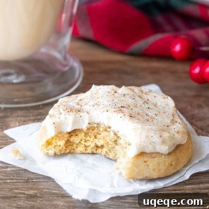 A beautifully frosted eggnog cookie with a bite taken out, showing the soft interior, paired with a glass of eggnog.
