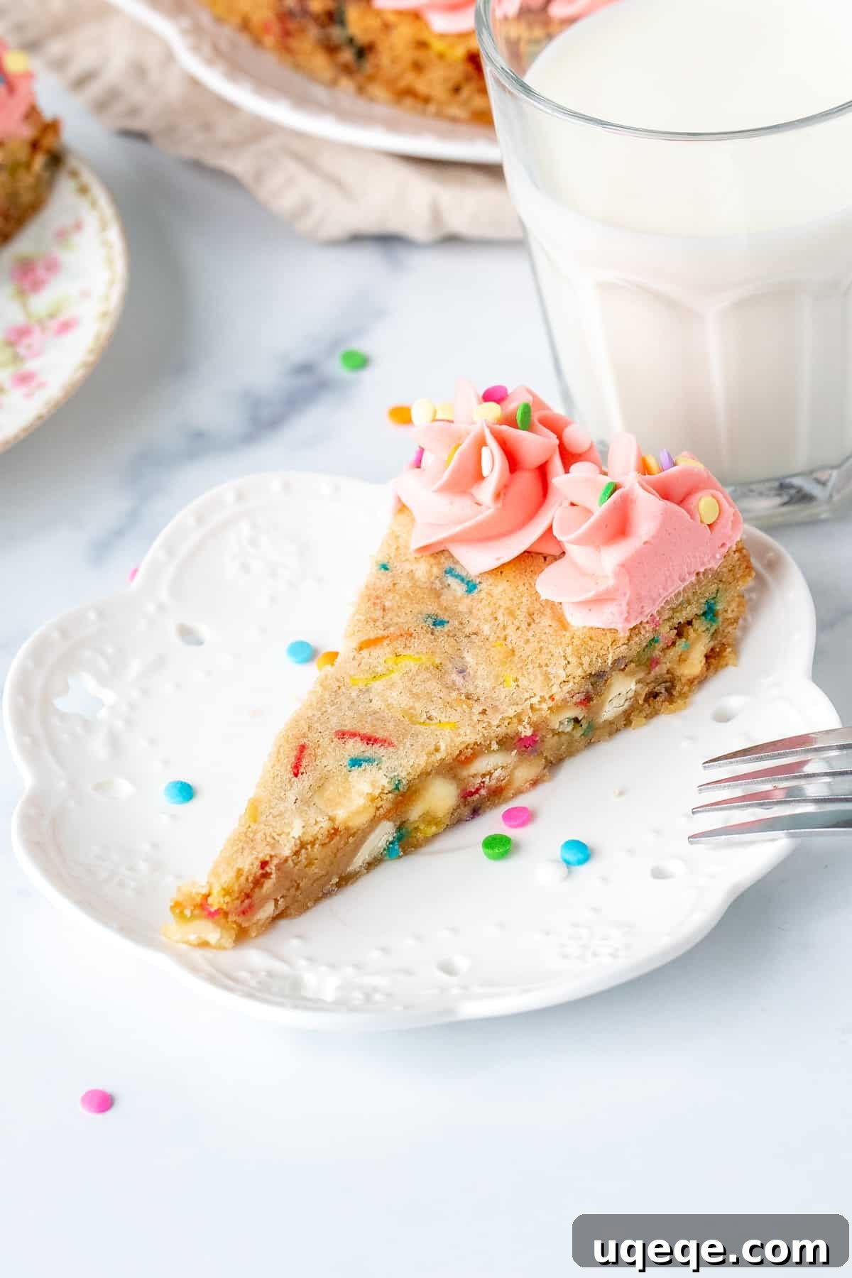 Celebration Sprinkle Cookie Cake 3 A perfectly baked slice of funfetti cookie cake adorned with a dollop of pink vanilla frosting, showcasing its chewy texture and abundant sprinkles.