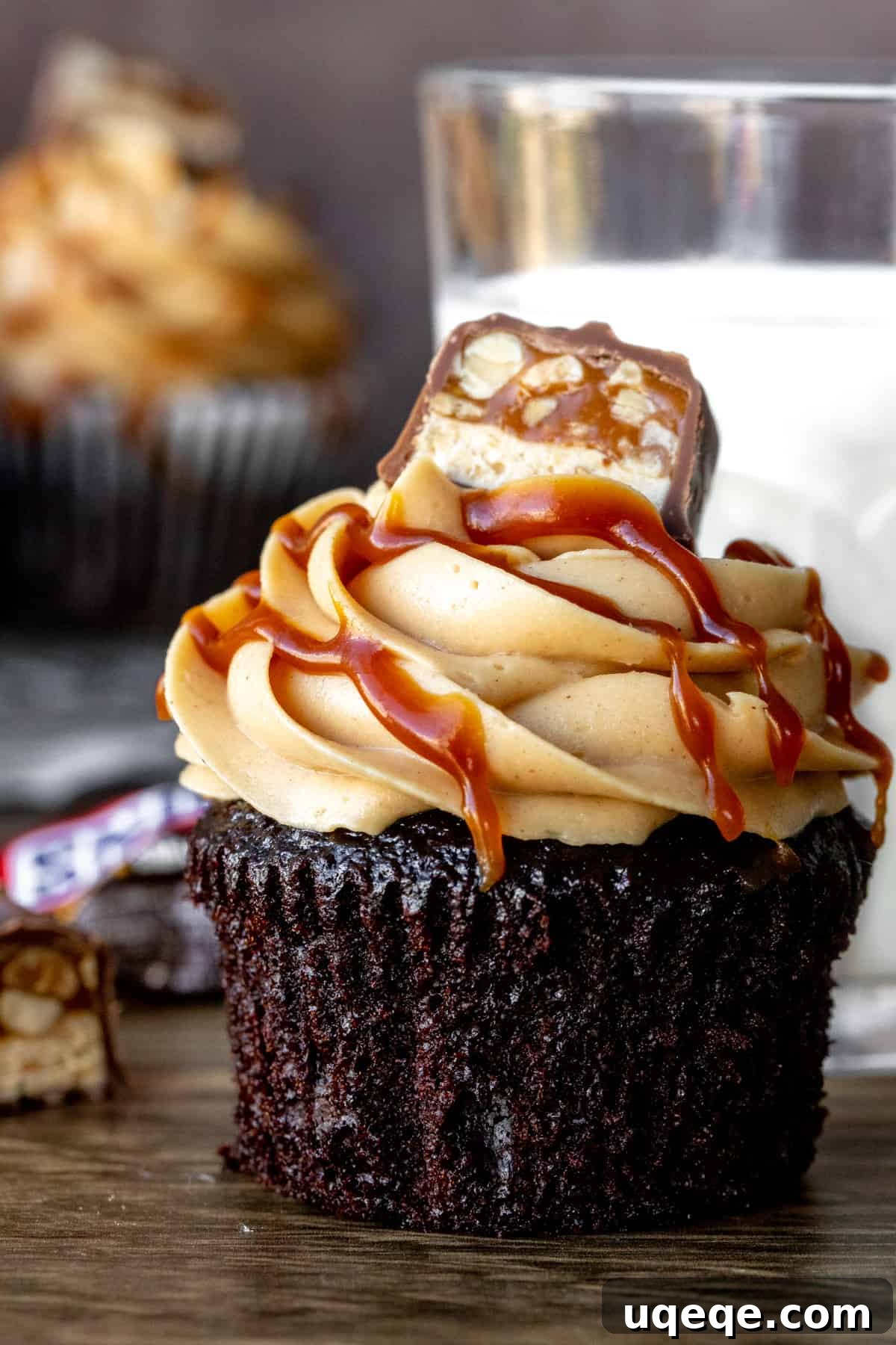 Snickers cupcakes with glass of milk, showcasing fudgy chocolate cake, creamy peanut butter frosting, caramel drizzle, and a Snickers chunk