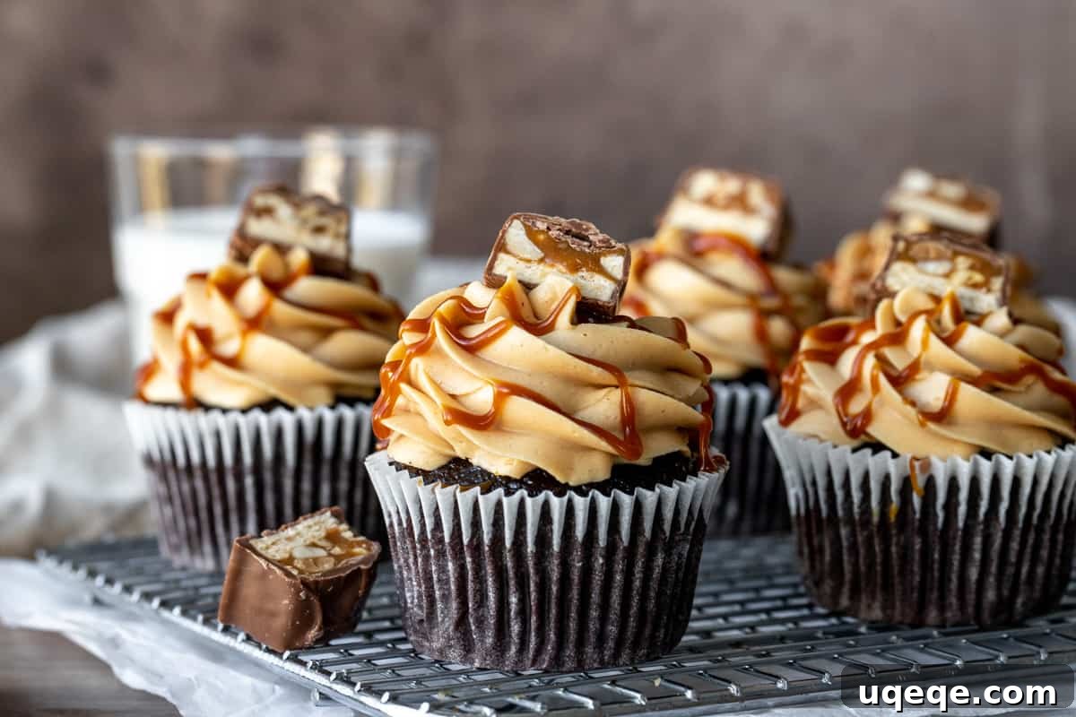 Cooling rack with freshly baked chocolate cupcakes topped with peanut butter frosting and a piece of Snickers bar