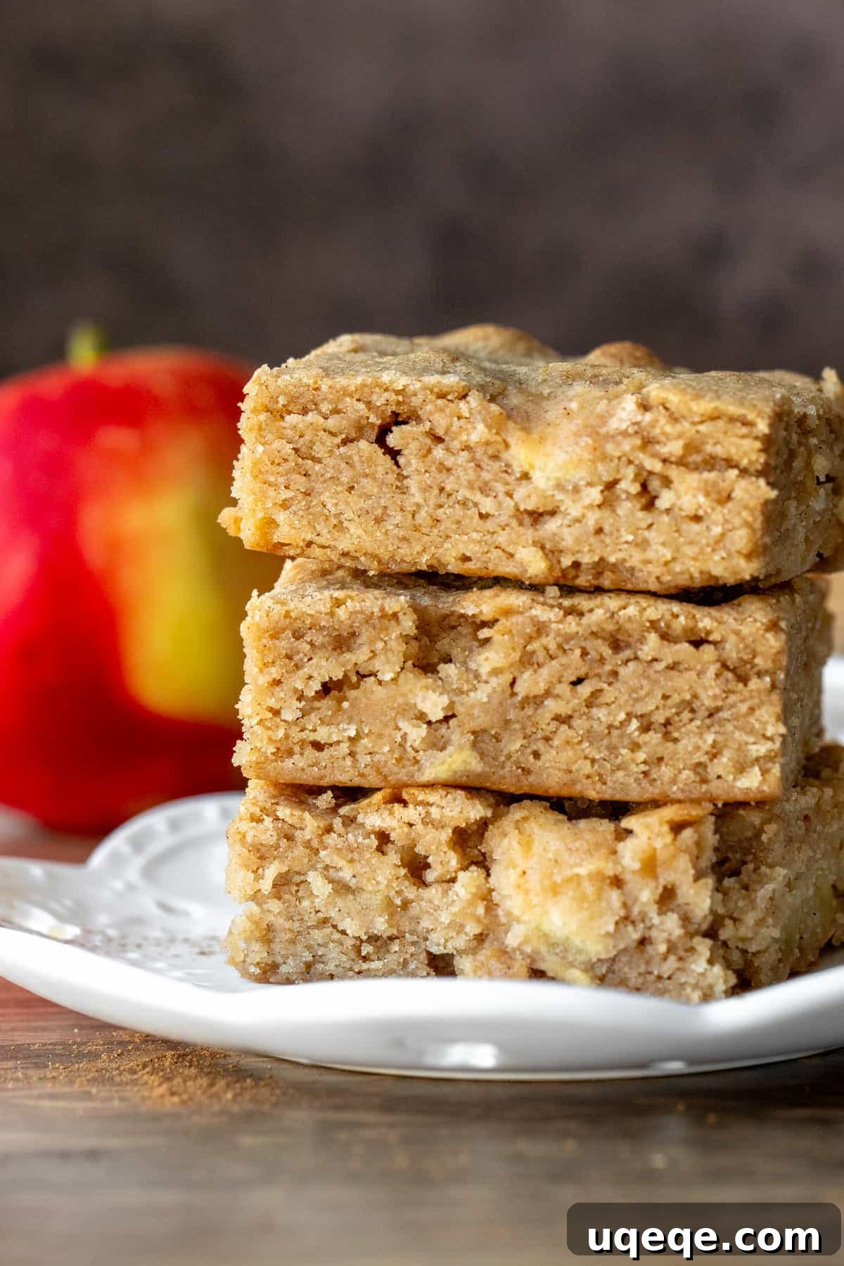 Three apple cinnamon blondies stacked one on top of the other on a white plate.