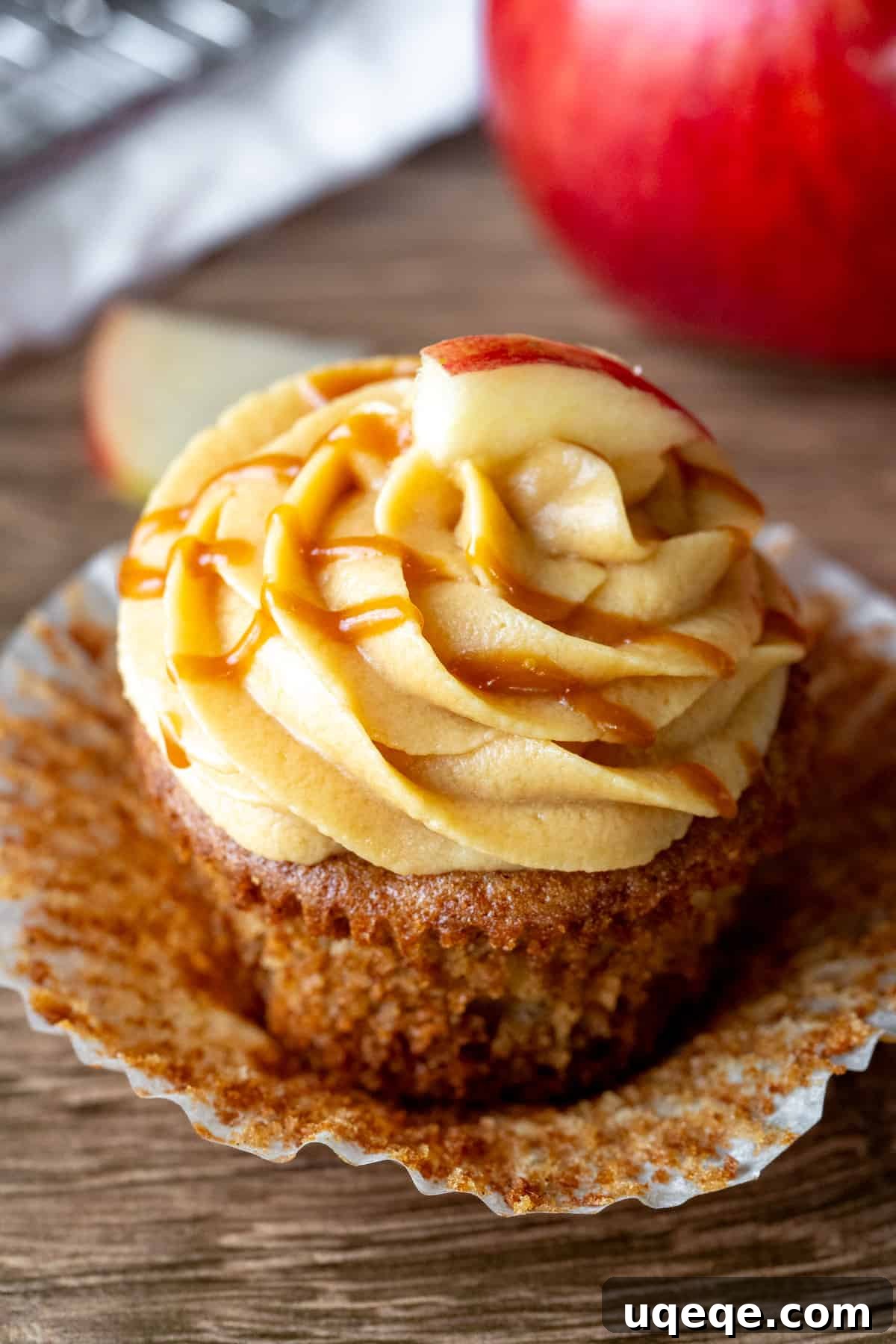 A beautifully frosted caramel apple cupcake with muffin paper peeled back, showcasing the moist apple cake, topped with creamy caramel cream cheese frosting and a luscious salted caramel drizzle.