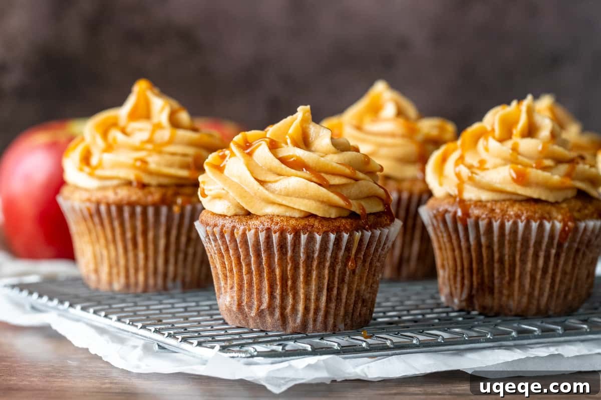 A wire rack filled with freshly baked apple cupcakes, cooling down and awaiting their delicious caramel cream cheese frosting.