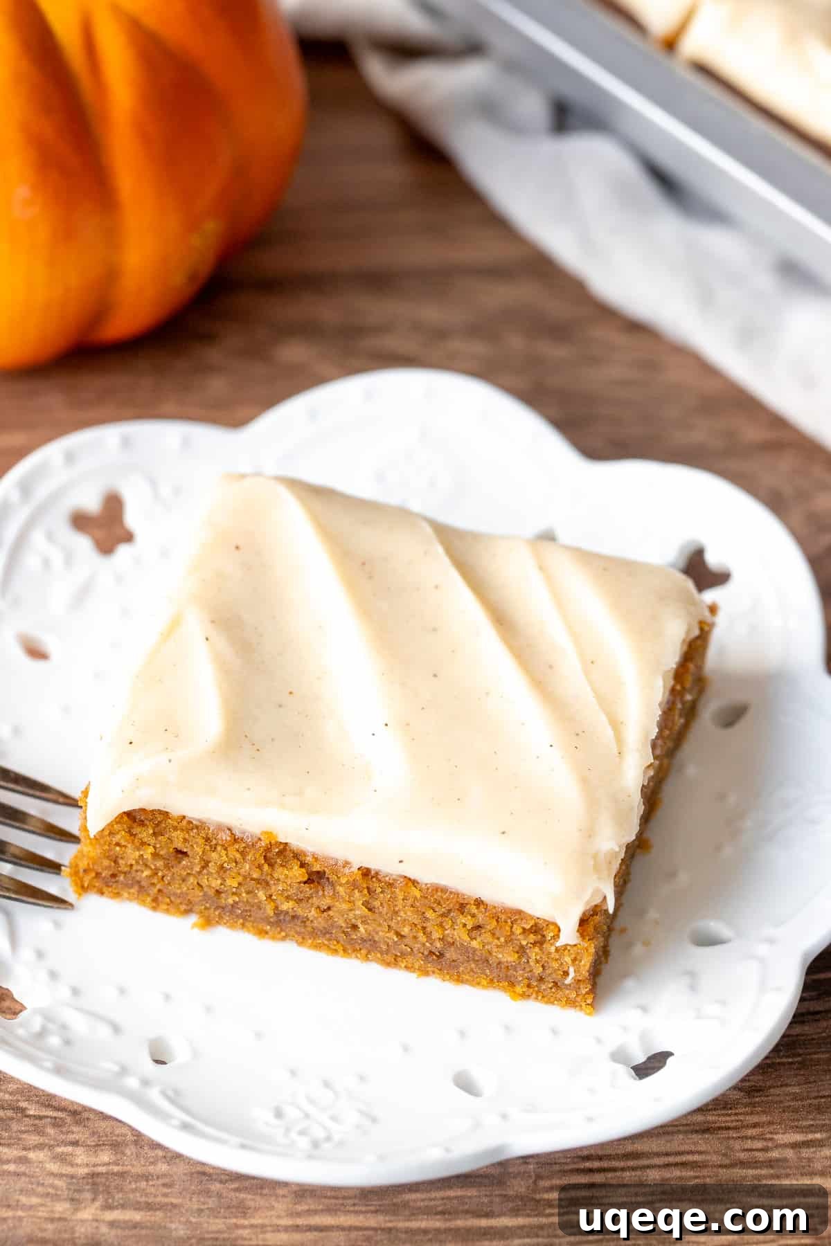Rich Pumpkin Bars with Spiced Cream Cheese Frosting 2 A single moist pumpkin bar with cinnamon cream cheese frosting on a white plate, ready to be enjoyed.