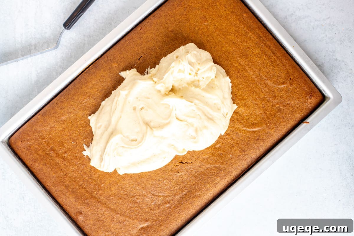 Rich Pumpkin Bars with Spiced Cream Cheese Frosting 6 A pan of baked pumpkin bars with dollops of creamy white cream cheese frosting spread unevenly over the top, waiting to be smoothed out.