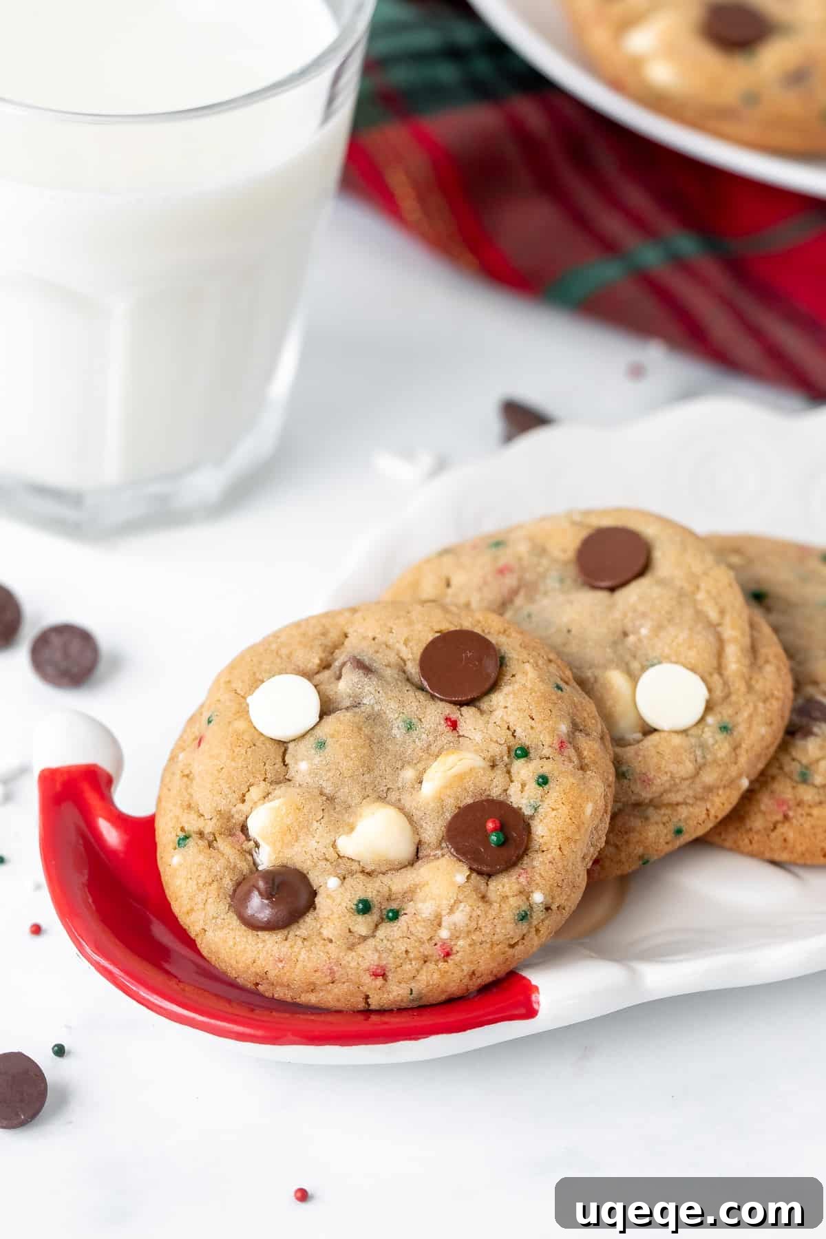A small Santa plate filled with festive Christmas chocolate chip cookies adorned with red and green sprinkles, accompanied by a glass of milk.