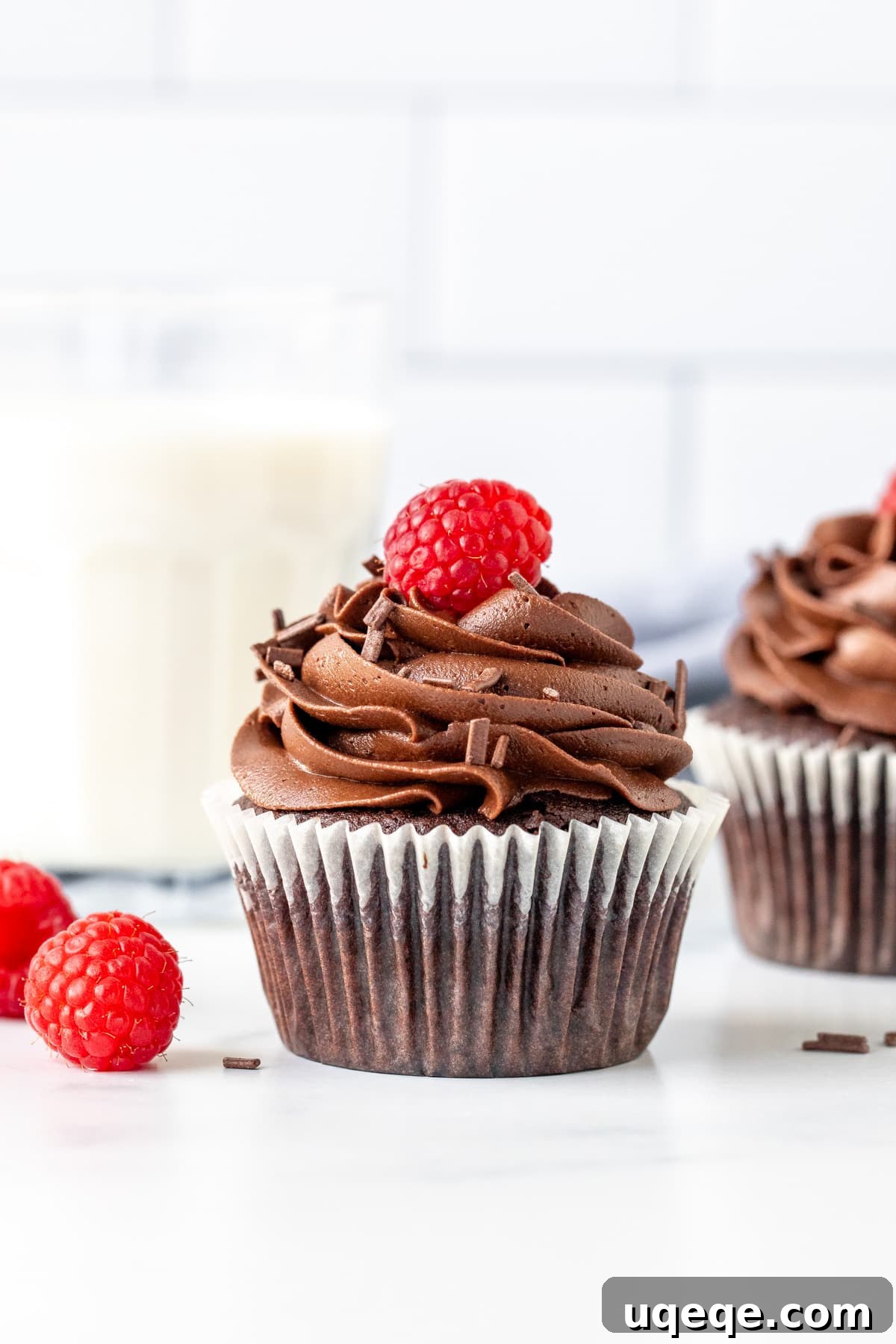 Perfect Pair Chocolate Cupcakes 3 A single chocolate cupcake, elegantly frosted and topped with a fresh raspberry, stands beside a glass of cold milk, inviting a delightful treat.