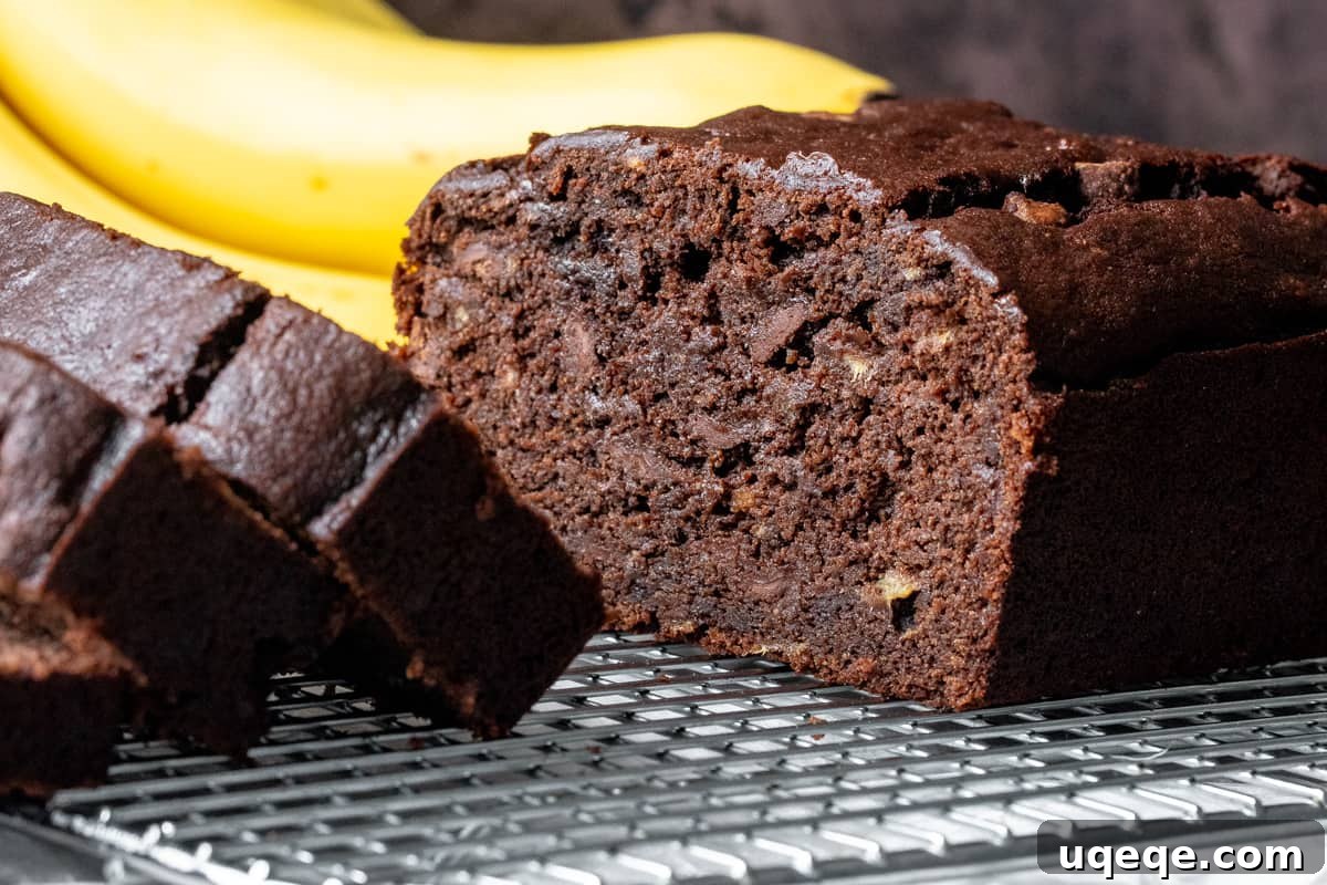 Decadent Double Chocolate Banana Bread 3 A freshly baked loaf of double chocolate banana bread, artfully cut in half to reveal its moist, chocolate-studded interior, flanked by a cluster of ripe, brown bananas.
