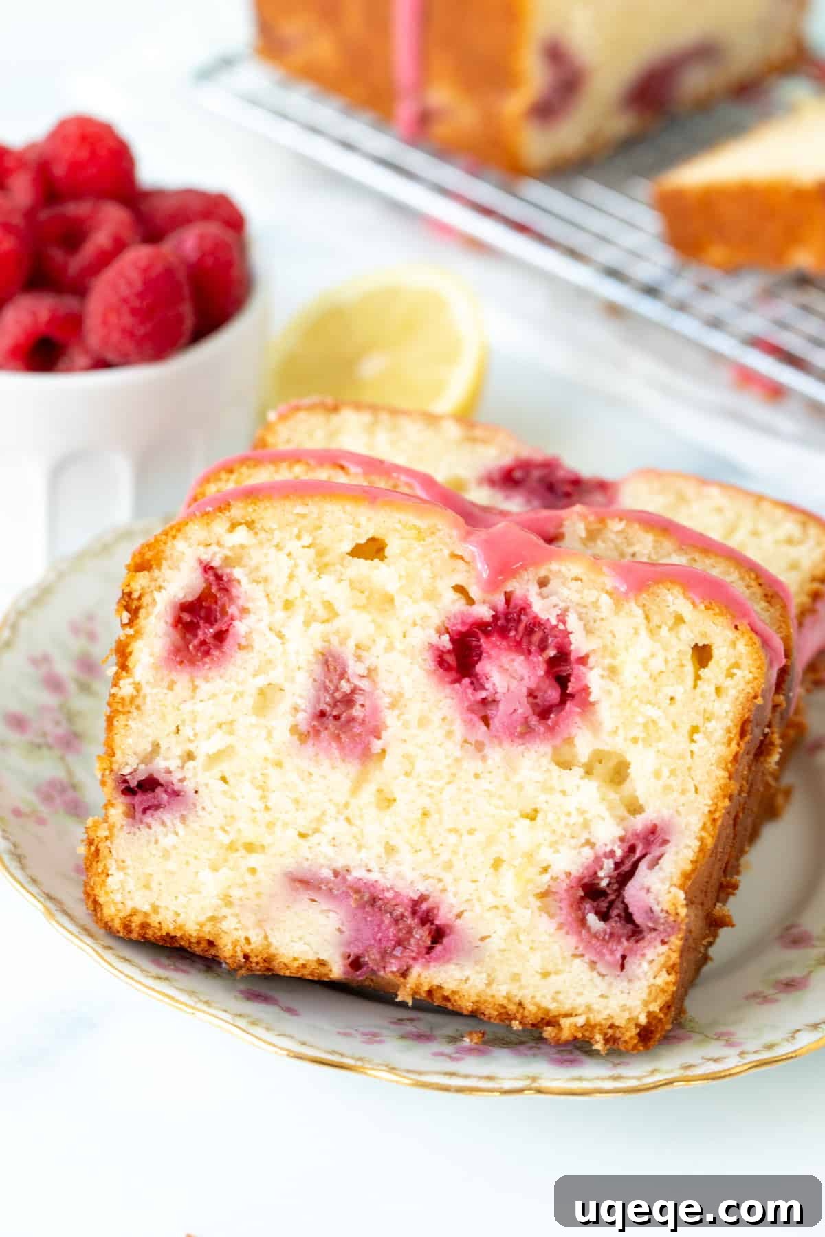 Lemon Berry Bliss Loaf 2 Slices of moist lemon raspberry loaf on a white plate, showcasing the berries and pink glaze