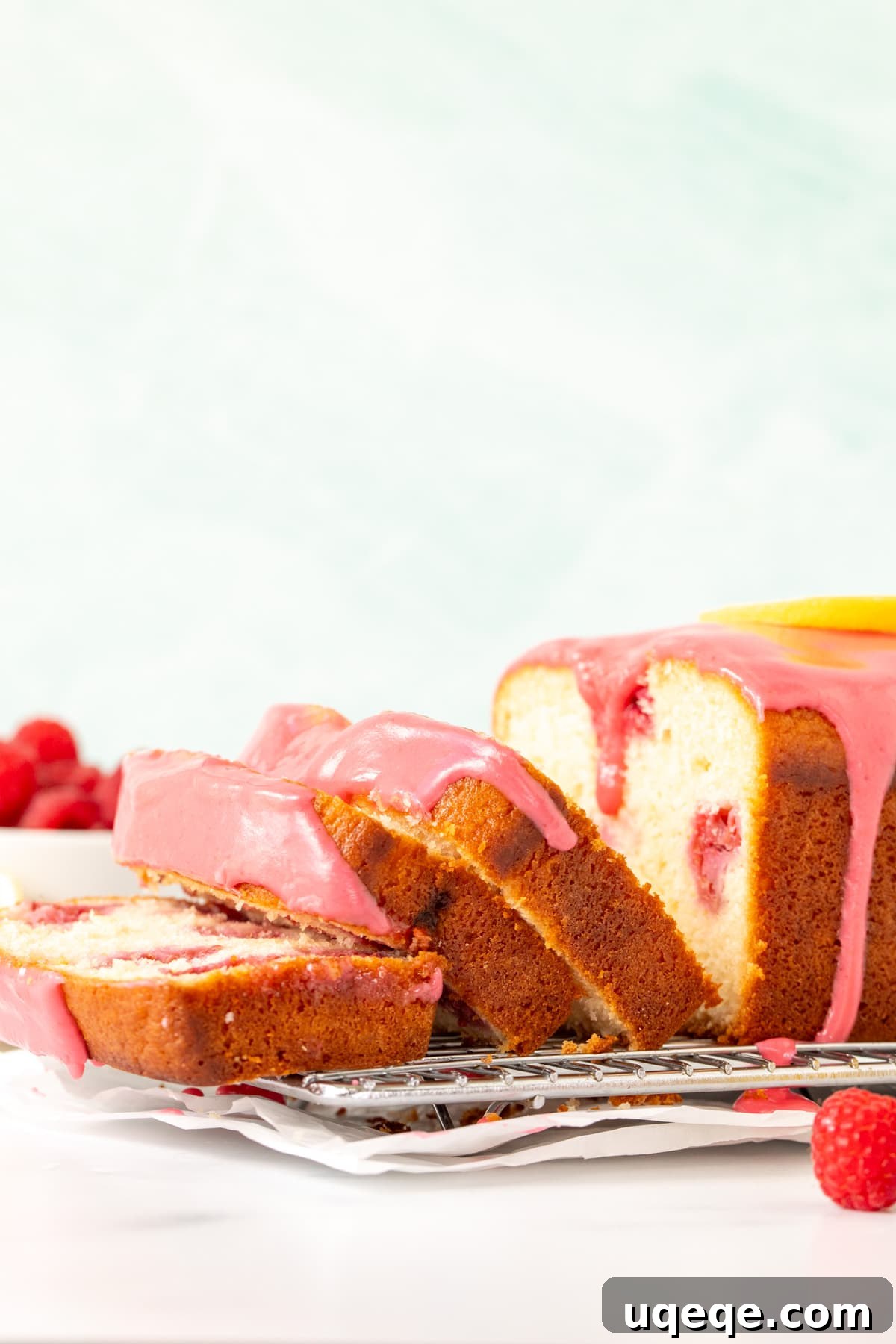 Lemon Berry Bliss Loaf 3 Freshly baked lemon raspberry bread on a cooling rack with three slices cut, revealing its moist interior and pink glaze.