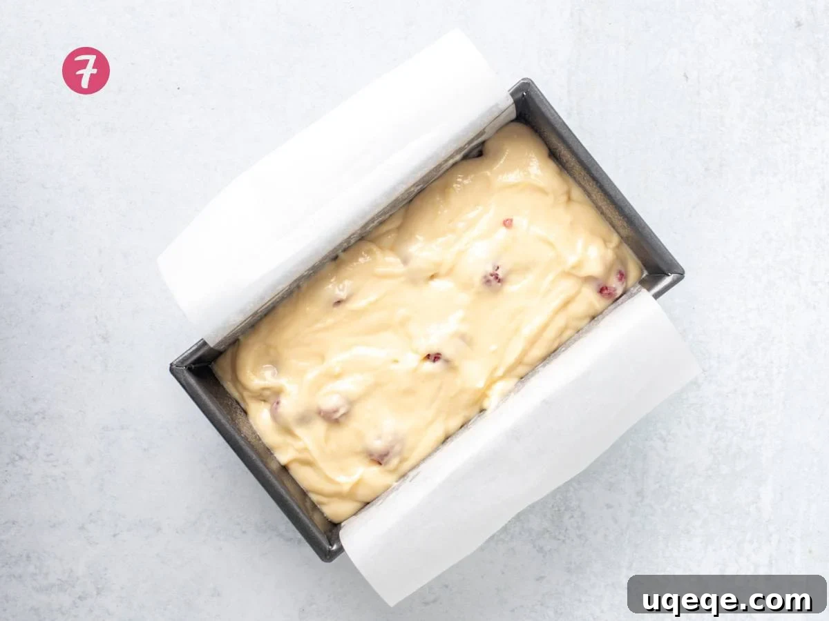 Lined loaf tin filled with unbaked lemon raspberry loaf batter and scattered raspberries.