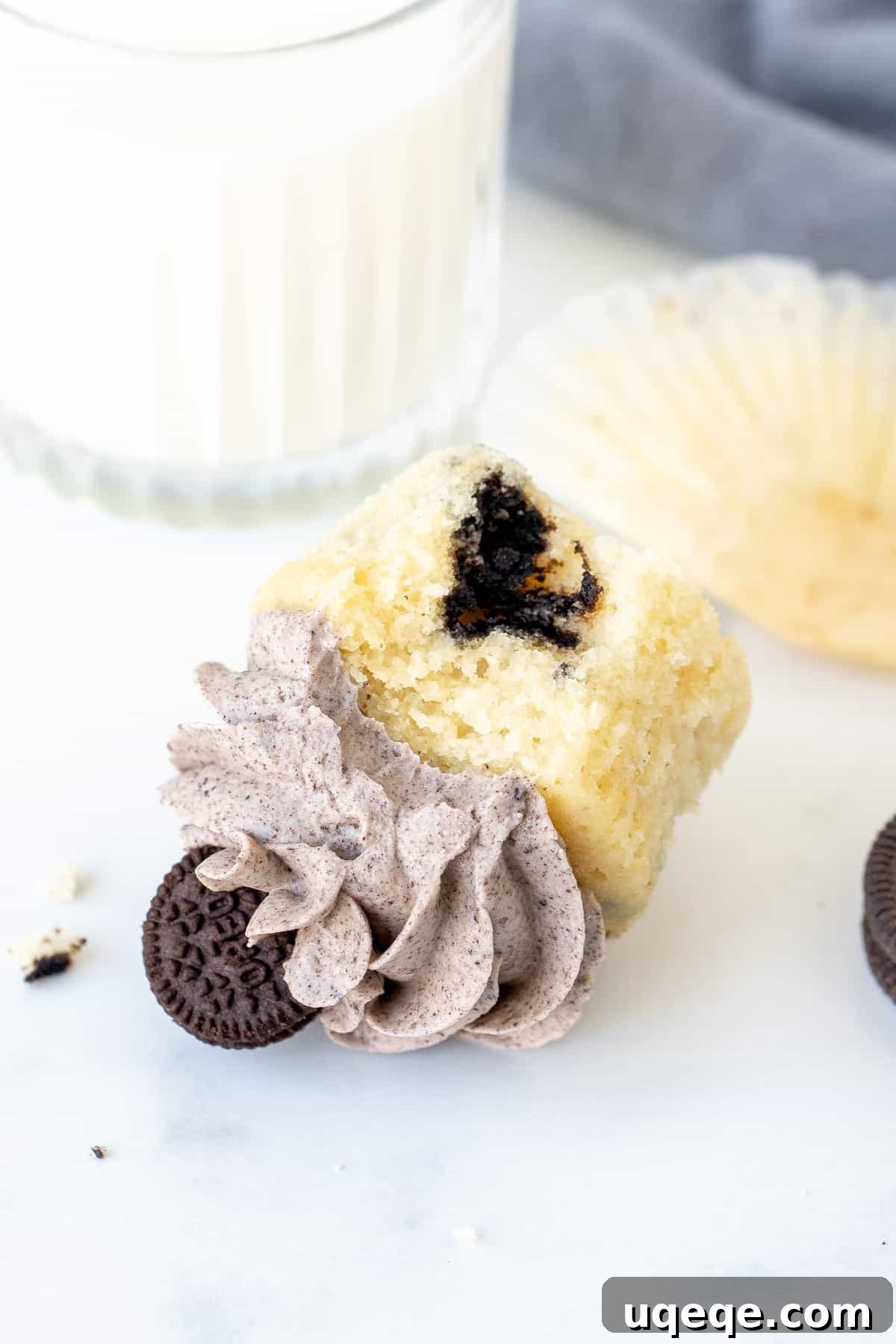 Oreo cupcake with a bite taken out, on its side with glass of milk