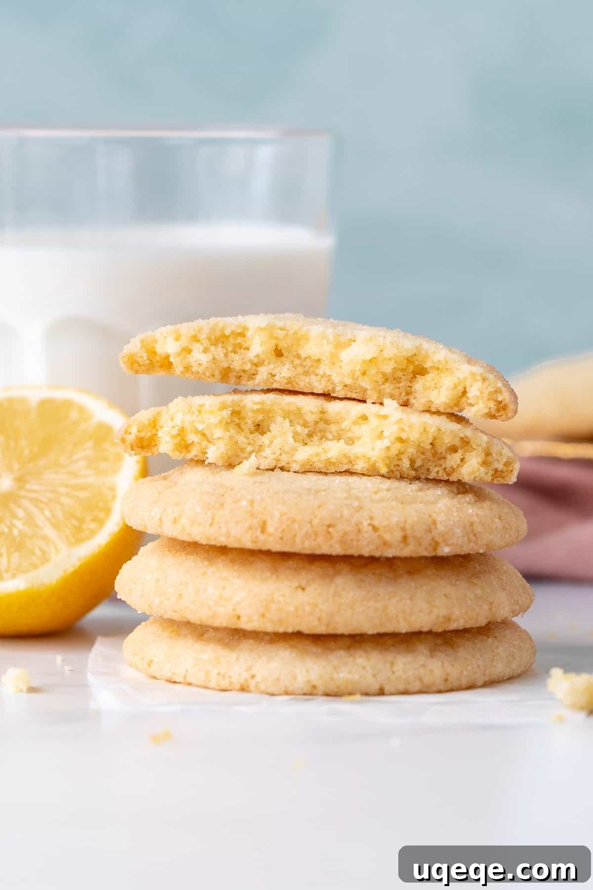 Zesty Lemon Delights 8 A stack of lemon sugar cookies, with the top cookie broken in half to reveal its soft, chewy interior texture.