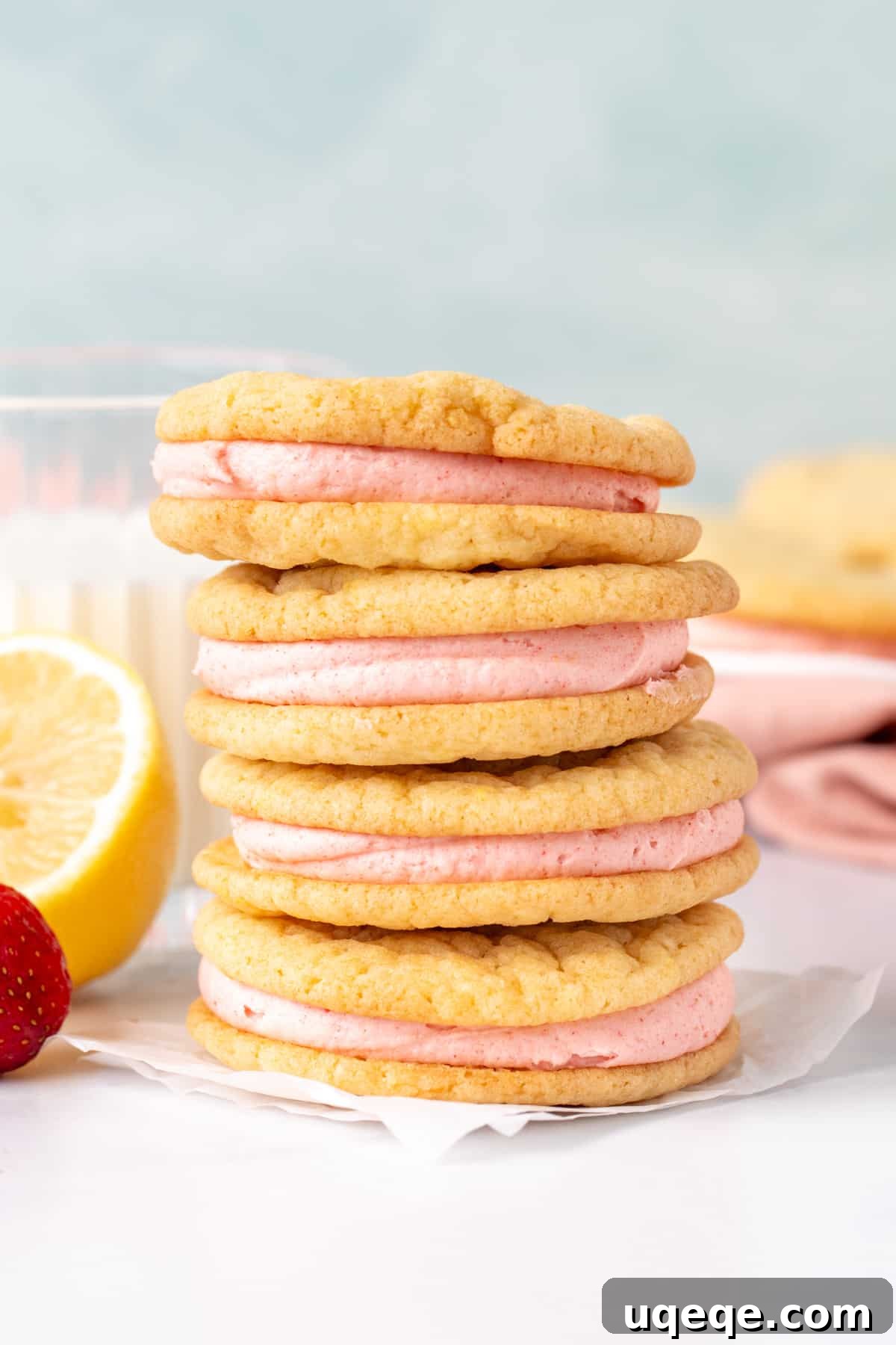 Stack of four lemon sandwich cookies, revealing luscious pink strawberry frosting in between layers