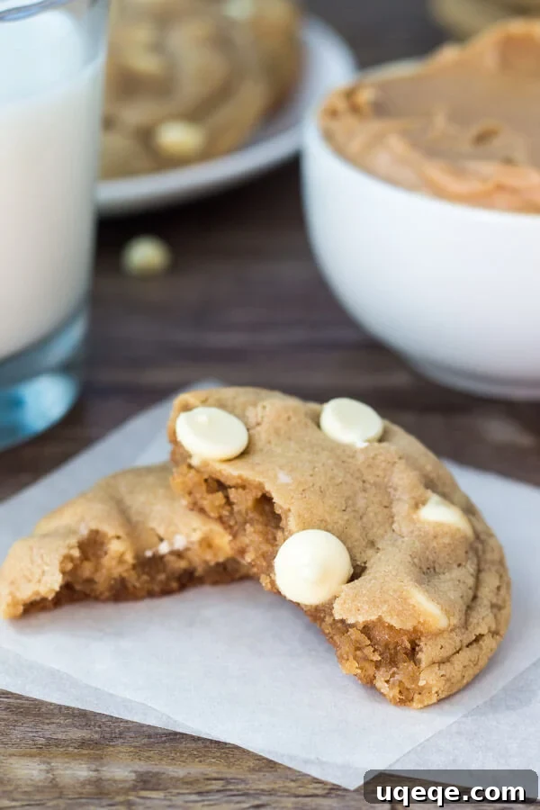 Peanut Butter White Chocolate Chip Delights 4 Peanut butter white chocolate chip cookie broken in half. Glass of milk and bowl of peanut butter in the background.