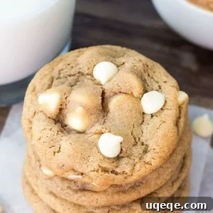 Overhead shot of a stack of peanut butter white chocolate chip cookies. Glass of milk and bowl of peanut butter in the background