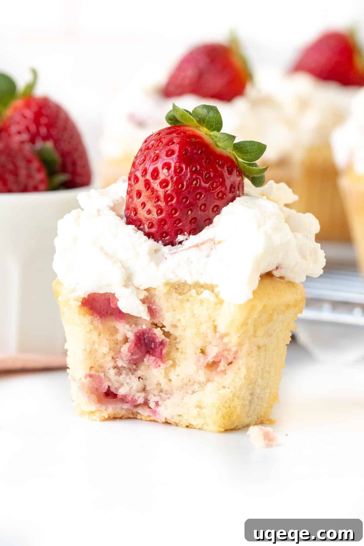 Luscious Strawberry Cream Cupcakes 3 A delectable strawberry cupcake topped with a generous dollop of whipped cream and a whole fresh strawberry, with a small bite taken out, showcasing the moist interior.