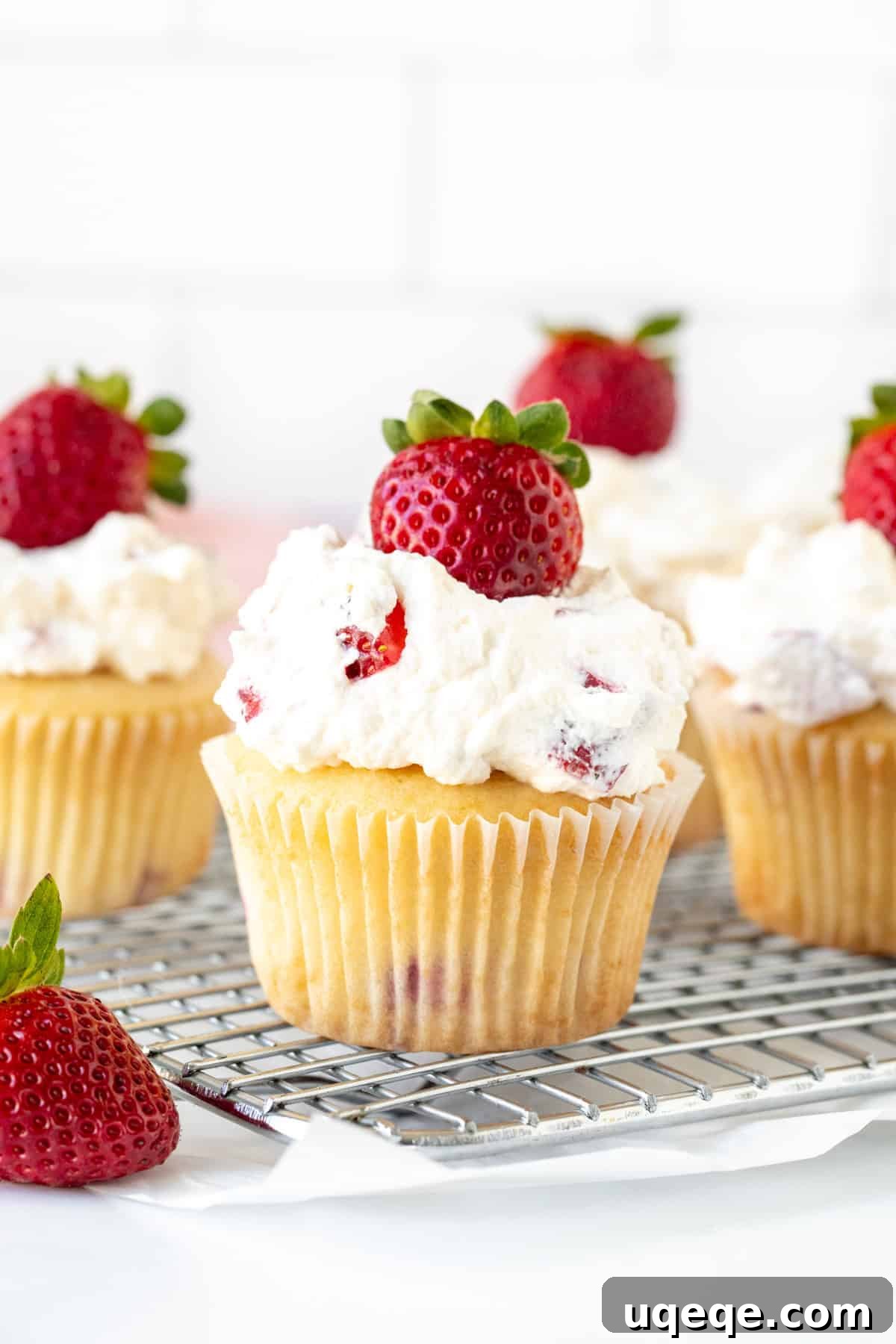 Luscious Strawberry Cream Cupcakes 4 An array of freshly baked strawberries and cream cupcakes, each adorned with a fresh strawberry, cooling on a wire rack.