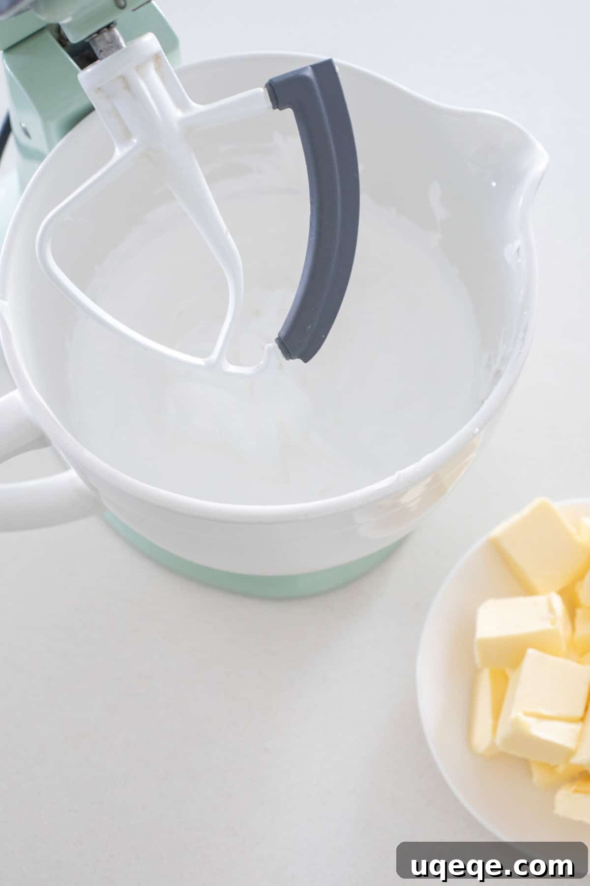 Silky Swiss Buttercream 5 Stand mixer with paddle attachment, bowl of meringue, and plate of cubed butter.