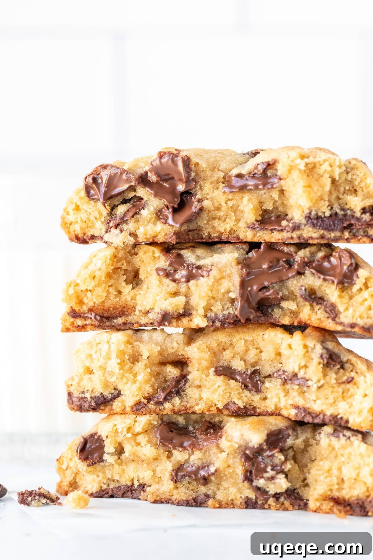 Chewy Chocolate Chip Cookies 2 A stack of four perfectly baked, thick chocolate chip cookies, each broken in half to reveal their gooey centers and an abundance of chocolate chips.