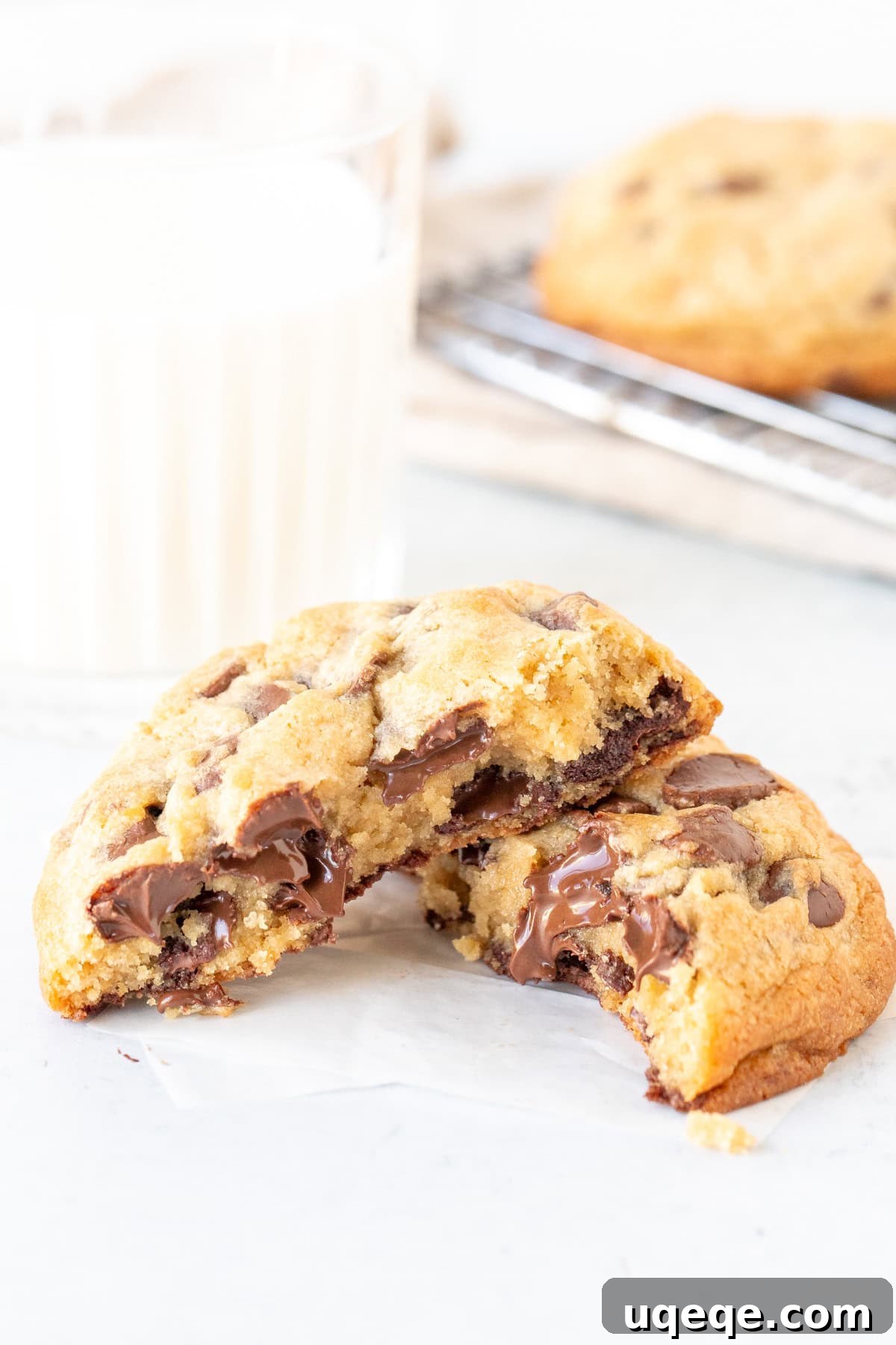 Chewy Chocolate Chip Cookies 3 A perfectly baked, extra thick chocolate chip cookie broken in half, revealing its incredibly gooey, chocolate-filled center, served alongside a refreshing glass of milk.