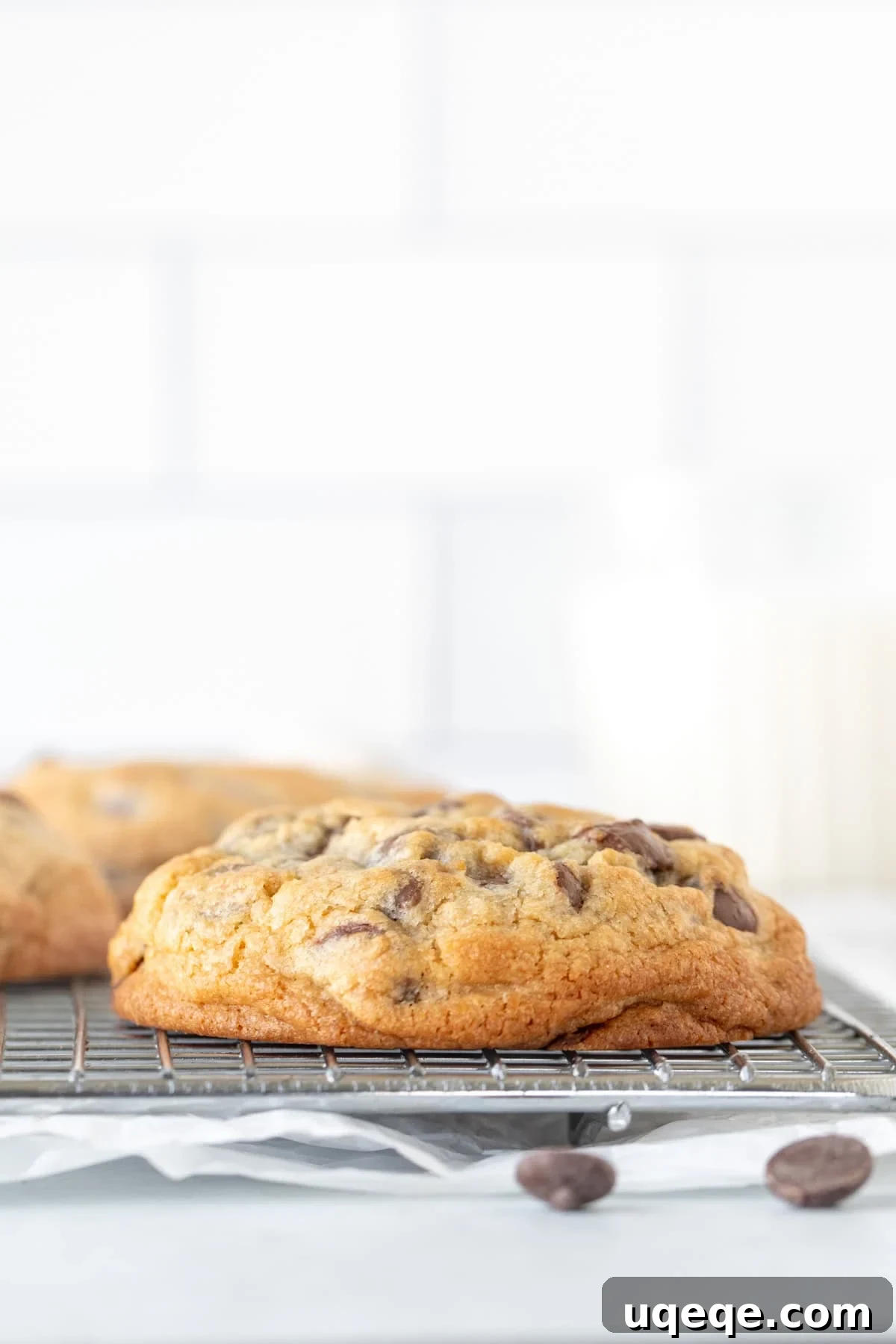 Chewy Chocolate Chip Cookies 8 A wire cooling rack filled with freshly baked, thick and chunky chocolate chip cookies, showcasing their golden-brown edges and substantial size, ready to be devoured.