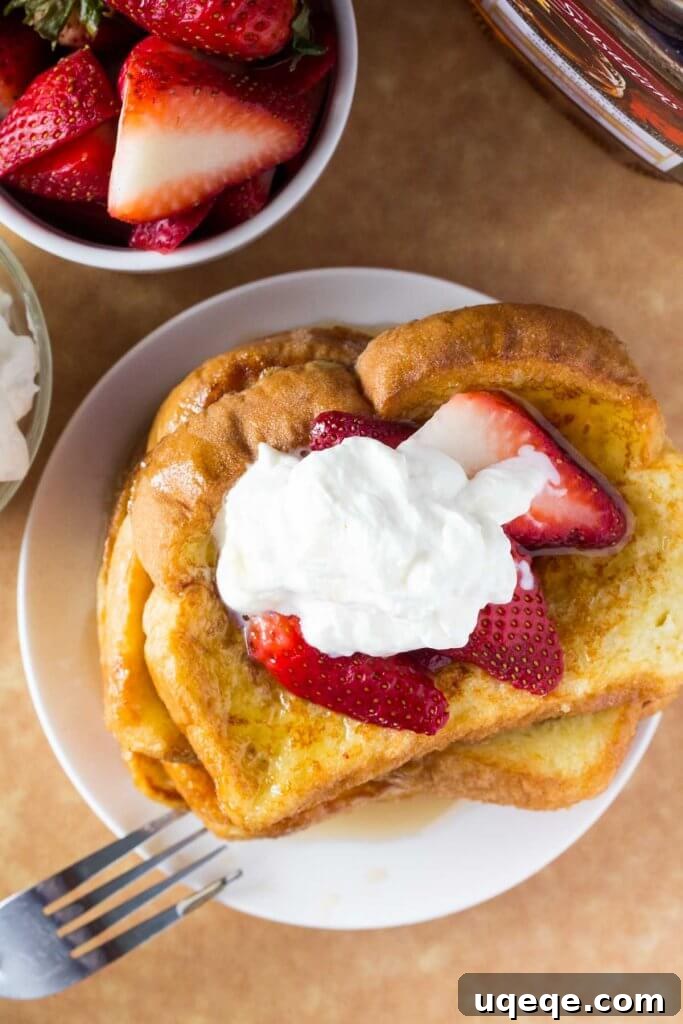 Overhead shot of a stack of golden French Toast with a bowl of strawberries and a bottle of maple syrup.
