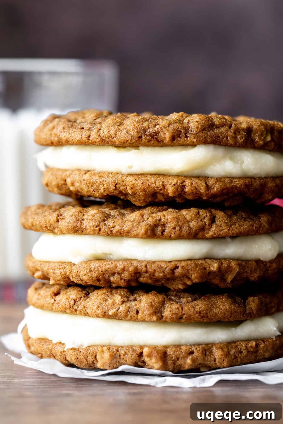 Spiced Gingerbread Oat Cream Dreams 3 Gingerbread oatmeal cream pie cookies, stacked invitingly with a glass of milk in the background, ready for a cozy treat.