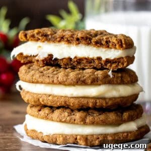 A close-up of a gingerbread oatmeal sandwich cookie, broken in half to reveal its creamy filling, stacked on other cookies.