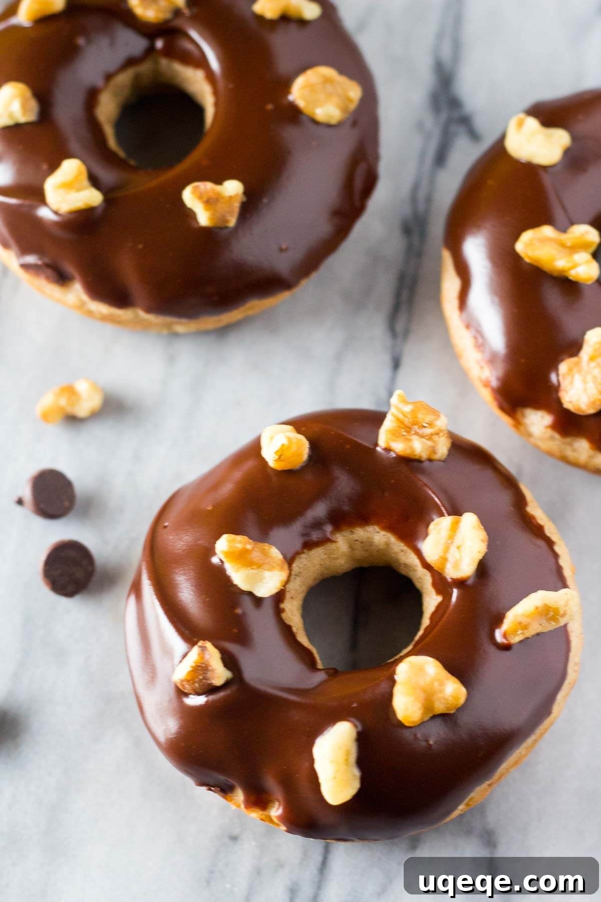 Beautifully arranged baked banana doughnuts with a shiny chocolate glaze and walnuts on top.