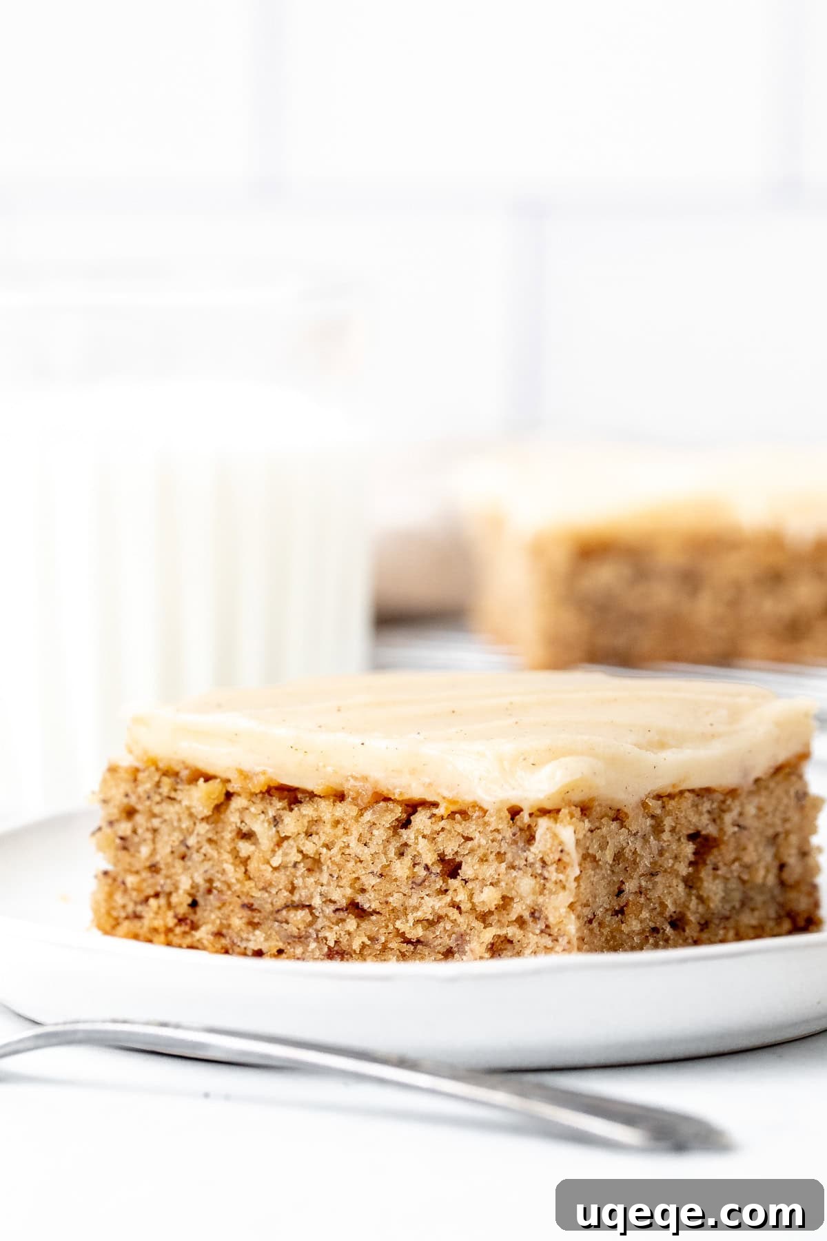 Frosted Banana Dream Bars 2 Moist banana bar with thick cinnamon cream cheese frosting, served on a white plate next to a glass of milk