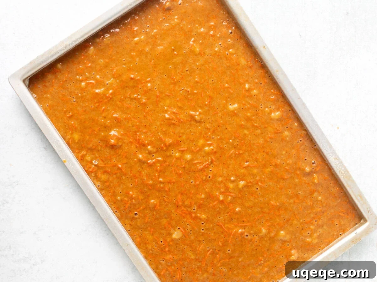 Spiced Carrot Cake Squares 6 An unbaked carrot cake bar batter spread evenly in a 10x15 inch jelly roll pan, ready to be placed in the oven.