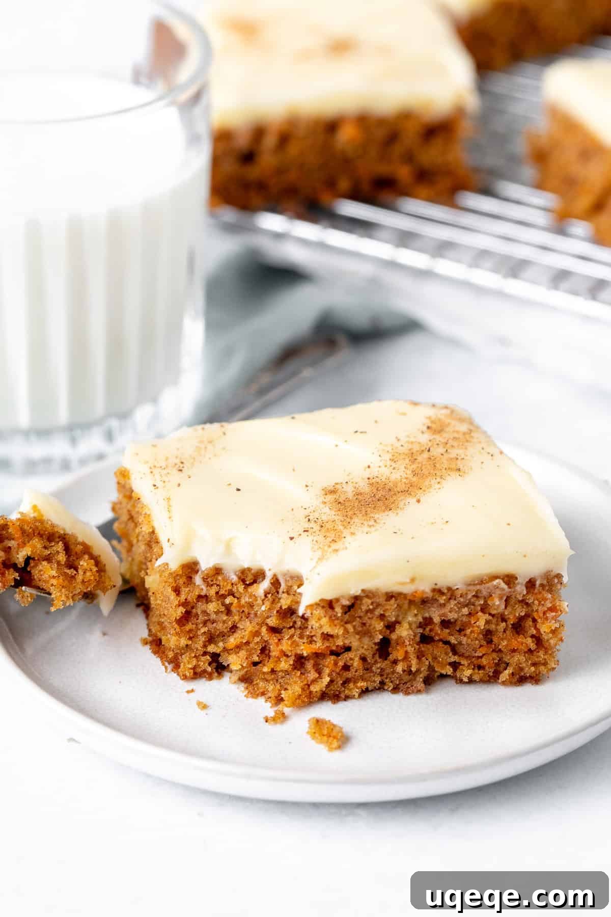 Spiced Carrot Cake Squares 8 A delicious slice of carrot cake bar with a bite taken out, showcasing the moist cake and thick cream cheese frosting, accompanied by a refreshing glass of milk.