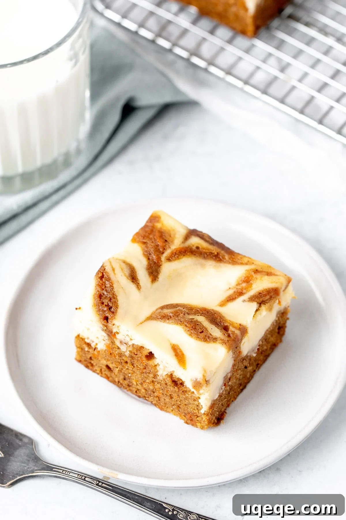 Spiced Carrot Cake Cheesecake Bars 2 Swirled carrot cake cheesecake bar on a plate with glass of milk, showcasing the beautiful marbled effect and inviting texture.
