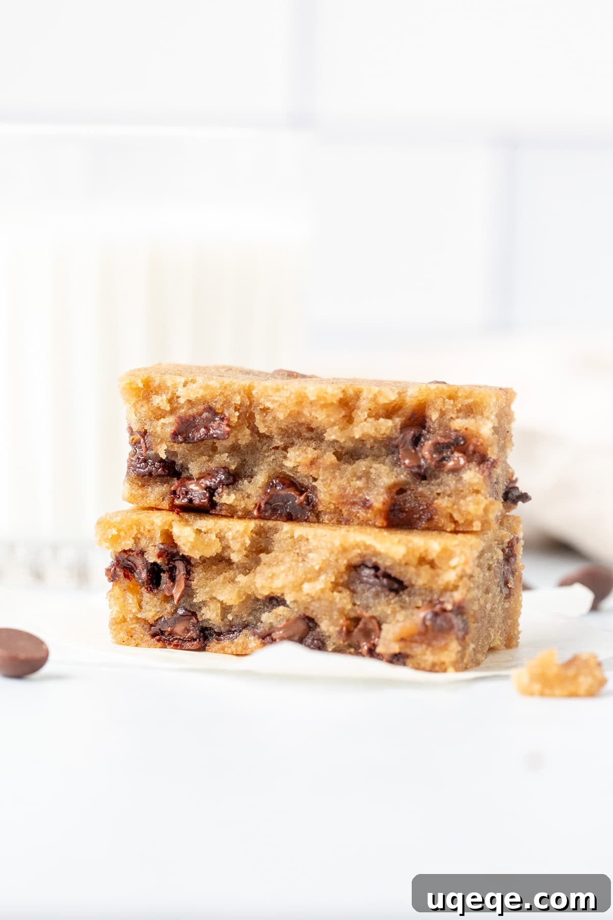Golden Banana Chocolate Chip Bars 7 A banana chocolate chip bar broken in half, revealing its moist, chocolatey interior, next to a glass of milk.
