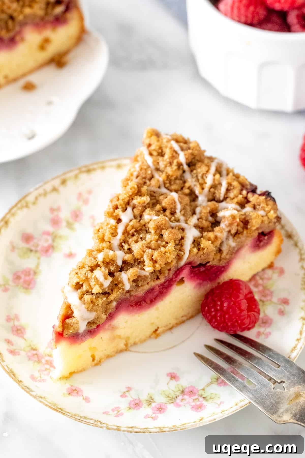A vibrant close-up of a slice of raspberry streusel coffee cake, highlighting the distinct layers of moist cake, juicy red raspberries, and golden-brown cinnamon crumb topping.