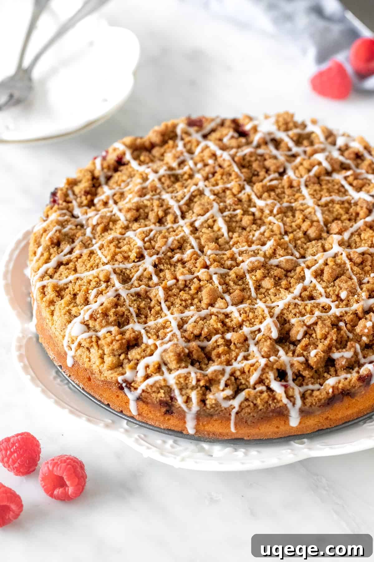 The full 9-inch round raspberry coffee cake, generously covered with cinnamon streusel and a delicate vanilla glaze drizzle, presented on a cooling rack.
