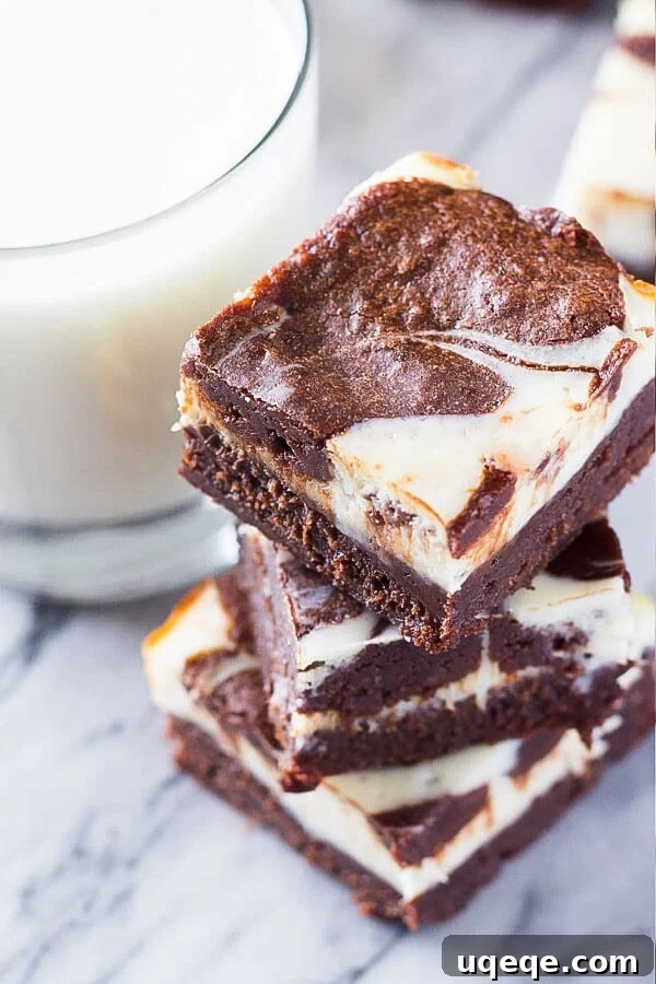 Swirled Cream Cheese Brownies 3 A stack of three perfectly cut cream cheese brownies next to a refreshing glass of milk, highlighting their inviting texture.