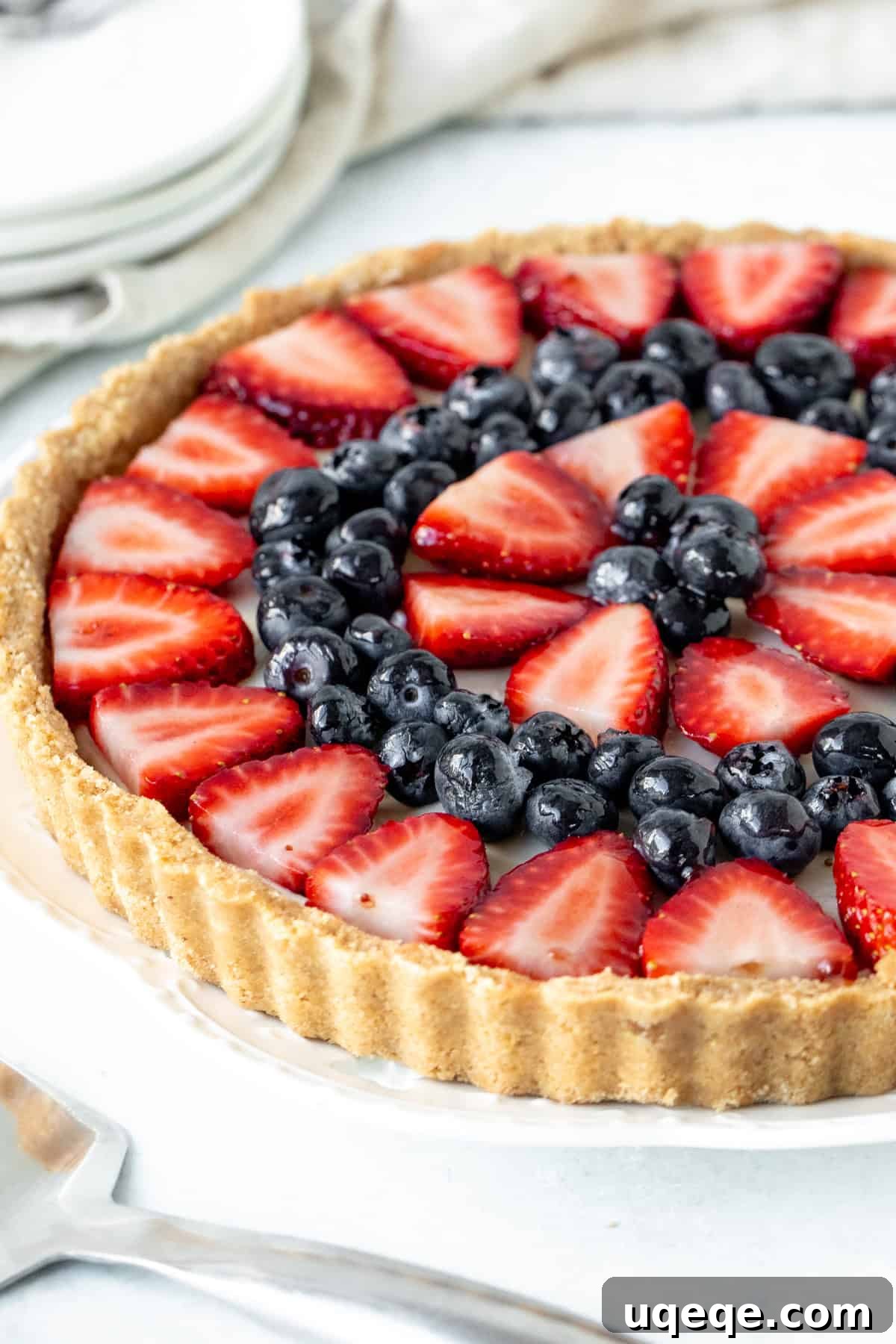 Effortless Rainbow Fruit Delight 2 Vibrant no-bake fruit tart with a golden graham cracker crust, topped generously with bright red strawberries and deep blue blueberries, presented on a rustic wooden board.