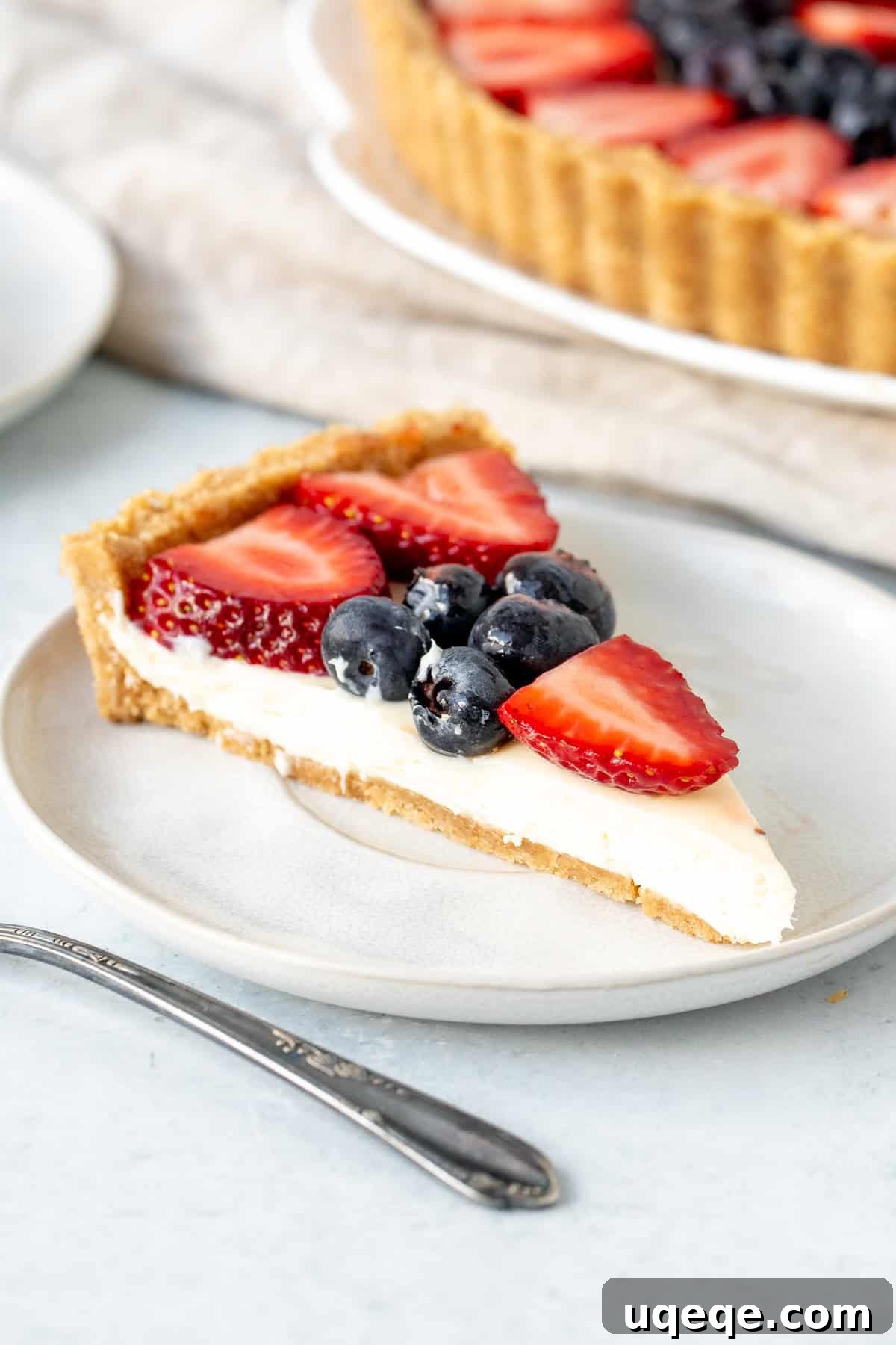 Effortless Rainbow Fruit Delight 3 A perfectly sliced portion of no-bake fruit tart revealing the crunchy graham crust, creamy white filling, and a topping of fresh berries, showing its irresistible layers.