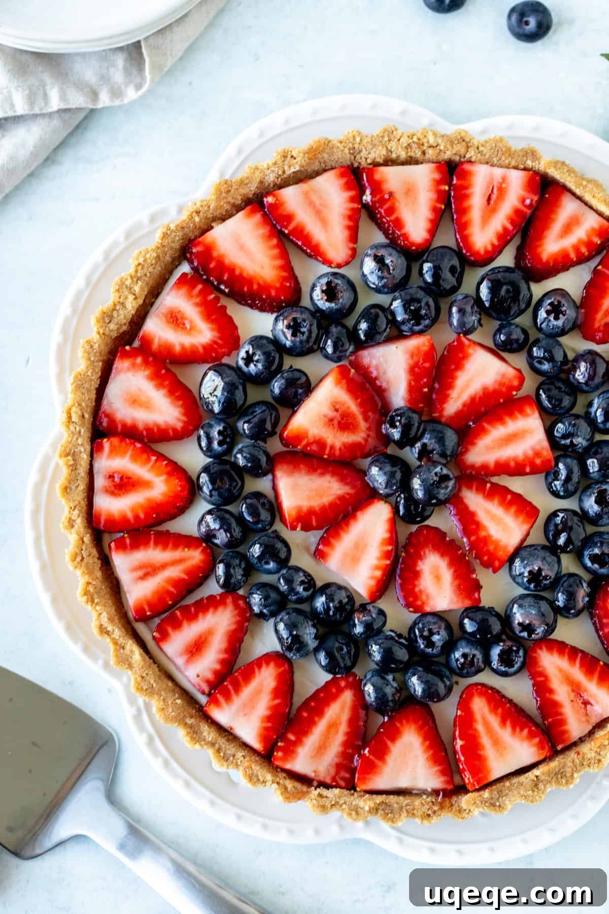 Effortless Rainbow Fruit Delight 8 A beautifully decorated fruit tart on a pristine white plate, generously topped with an artful arrangement of bright blueberries and perfectly sliced strawberries, showcasing its fresh appeal and ready to be served.