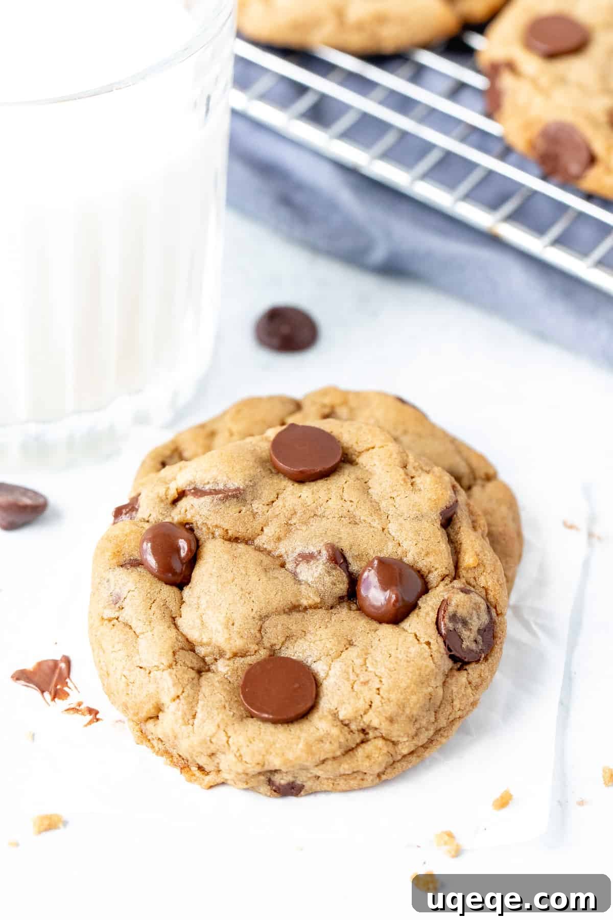 Dreamy Cream Cheese Chocolate Chip Cookies 7 A soft, gooey chocolate chip cookie resting on another, with a glass of milk in the background.