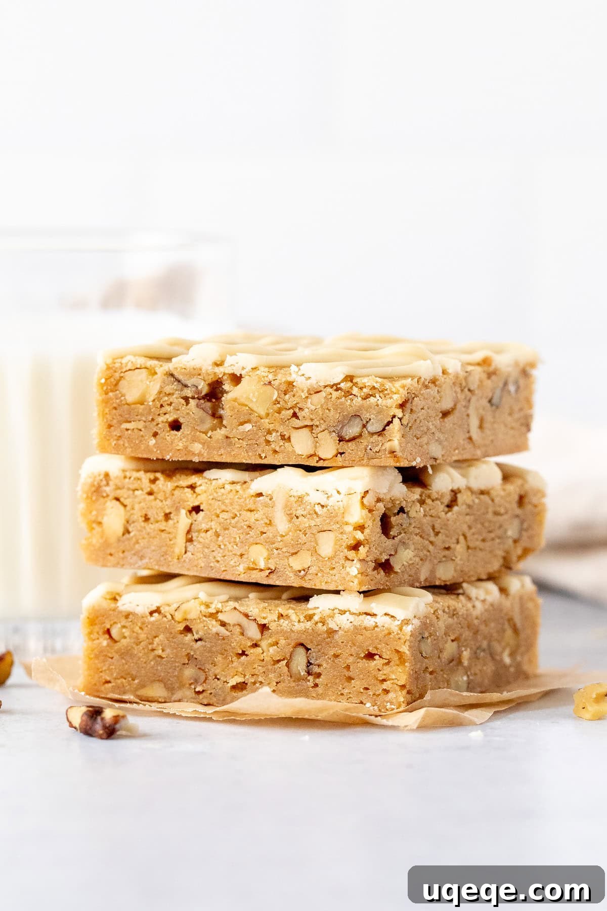 Golden Brown Butter Maple Blondies 2 Stack of three maple blondies, drizzled with glaze and garnished with chopped nuts, on a white background.