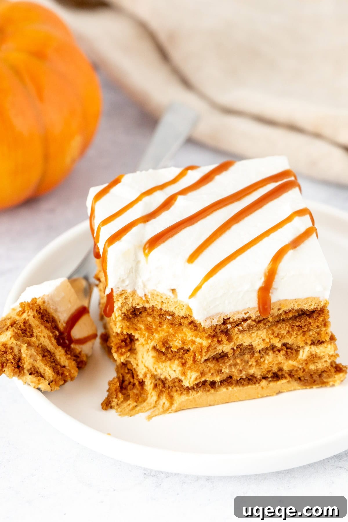 A top-down view of the pumpkin icebox cake, showing distinct layers of soft Lotus Biscoff cookies and creamy no-bake pumpkin cheesecake filling, beautifully topped with whipped cream and caramel drizzle.