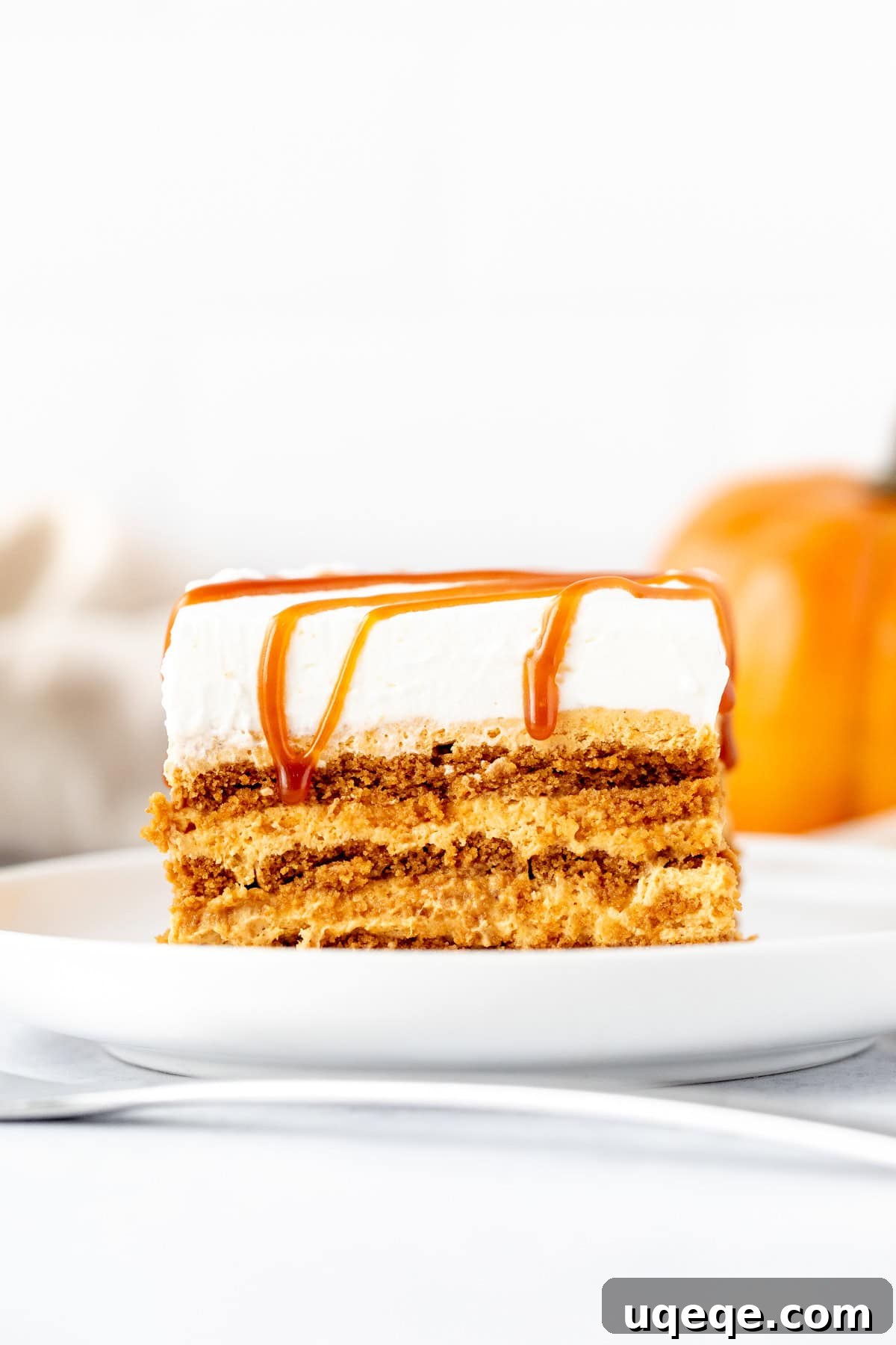 Close-up shot of a perfect slice of pumpkin icebox cake on a white plate, showcasing the distinct layers of cookie and creamy filling, with a luscious whipped cream and caramel topping.