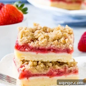 Stack of 2 strawberry crumb bars on white plate with bowl of strawberries.