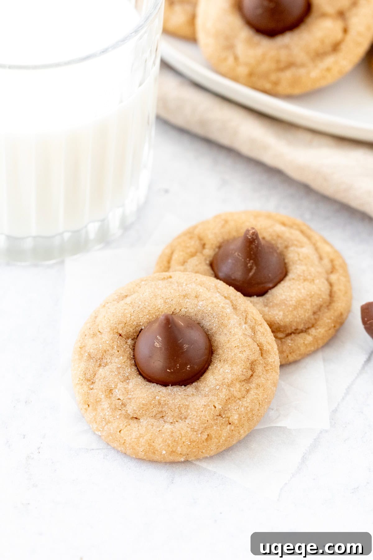 Peanut Butter Bliss Bites 4 Two freshly baked peanut butter chocolate kiss cookies sit invitingly beside a tall glass of cold milk, capturing a classic pairing.