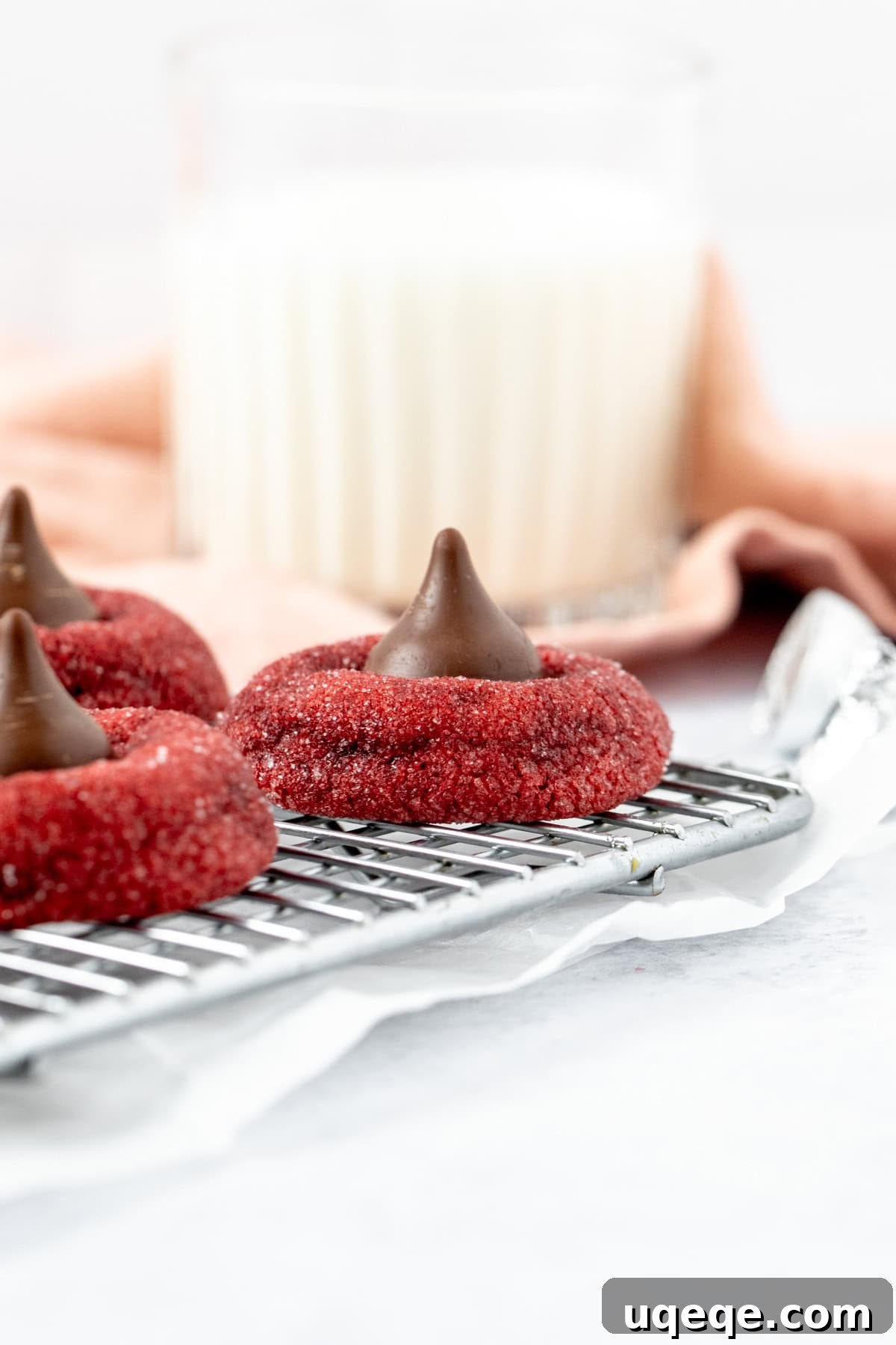 Crimson Unfurl 3 Red velvet Hershey's Kiss cookies on a cooling rack with a glass of milk