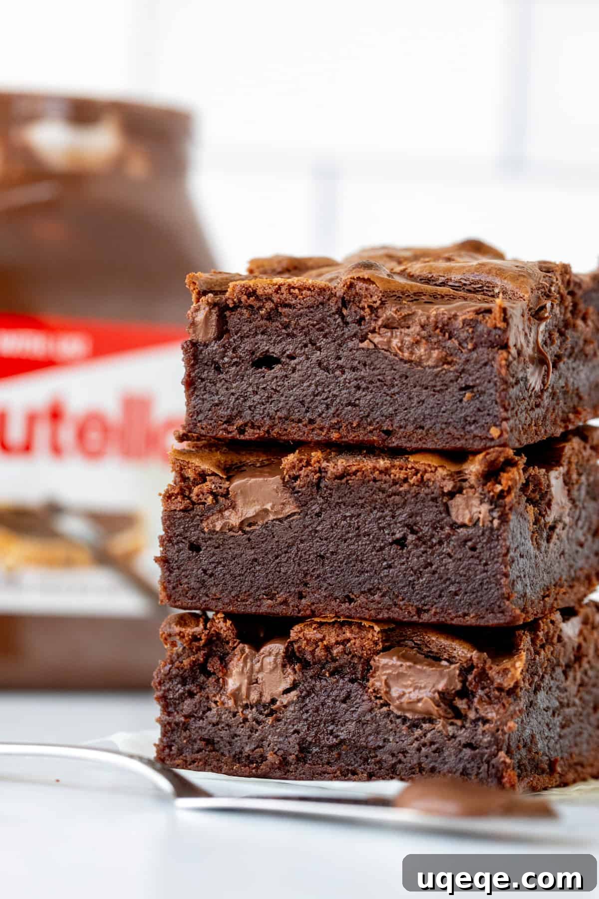 Decadent Nutella Fudge Brownies 2 Stack of three incredibly fudgy Nutella brownies with a jar of Nutella in the background