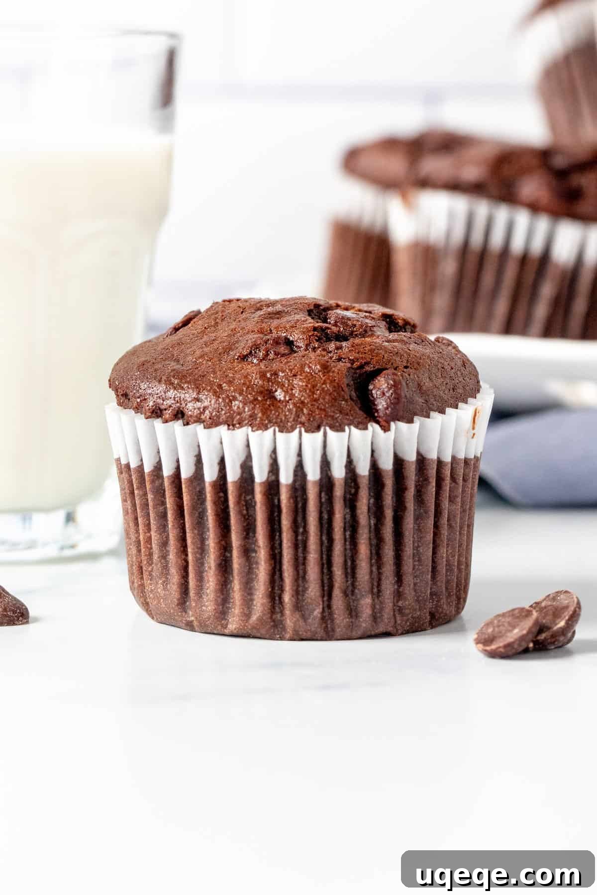 Ultimate Double Chocolate Banana Muffins 6 A chocolate banana muffin paired with a glass of milk, with a plate of more muffins in the background